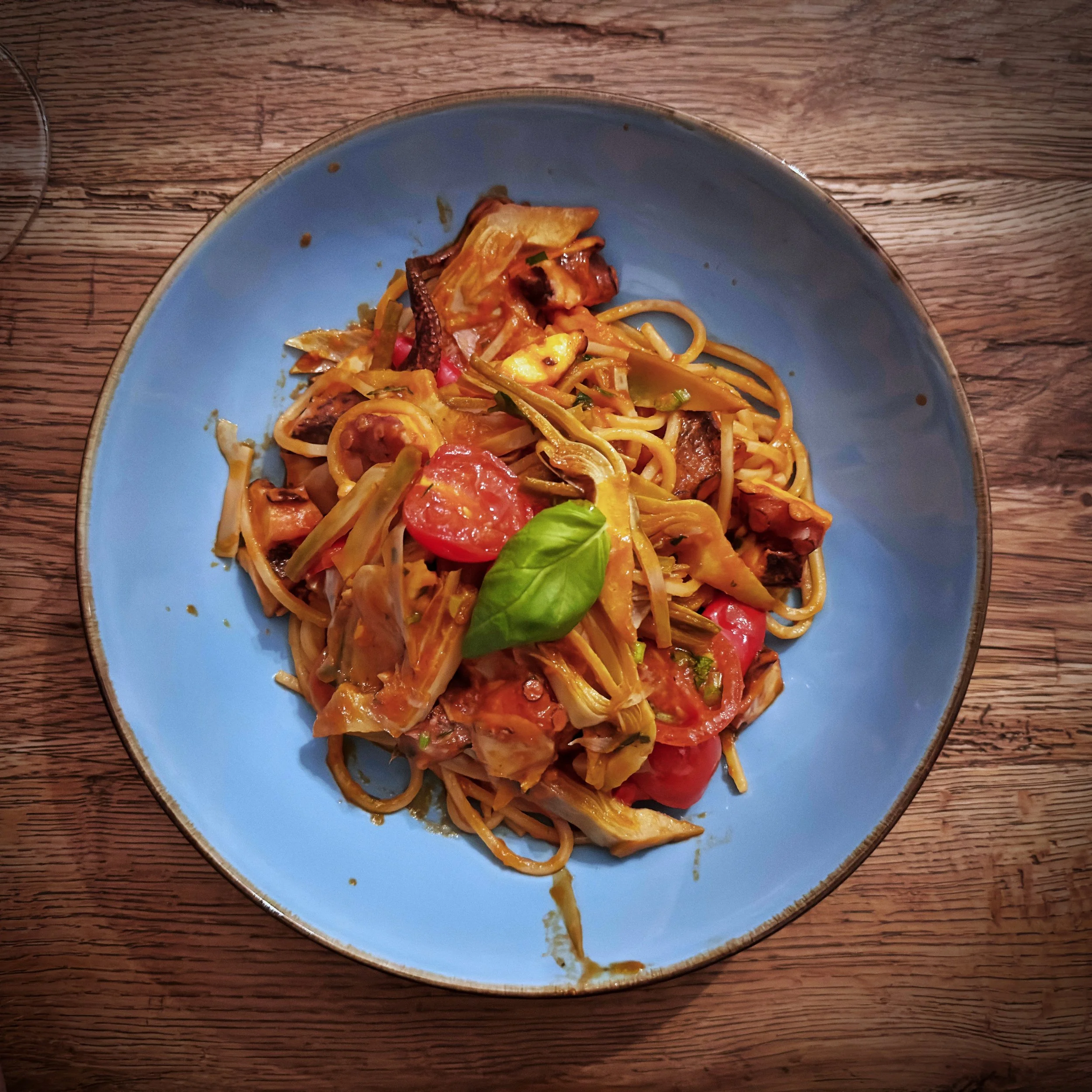 Spaghetti mit Tintenfisch, Kirschtomaten, Artischocken und Basilikum in einer blauen Schüssel auf einem Holztisch im Il Piccolo Principe in München.