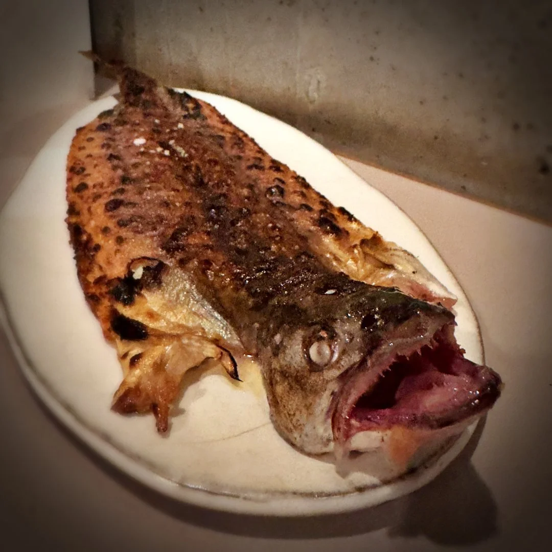 Ein ganzer Bachsaibling mit gegrillter Haut auf einem ovalen Teller im Restaurant Otto in Berlin. Der Fisch stammt von regionalen Fischereien und steht für Vadims Fokus auf das pure Produkt.