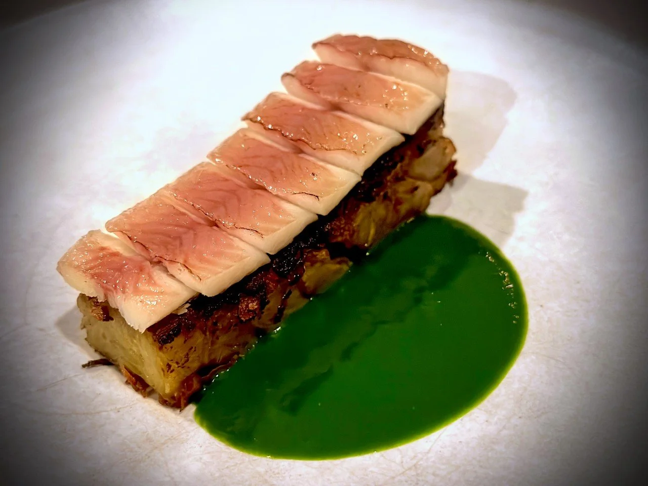 smoked fish on a  potato terrine, served with an intense green sauce at Otto restaurant in Berlin. The minimalist arrangement highlights the restaurant's modern food concept.