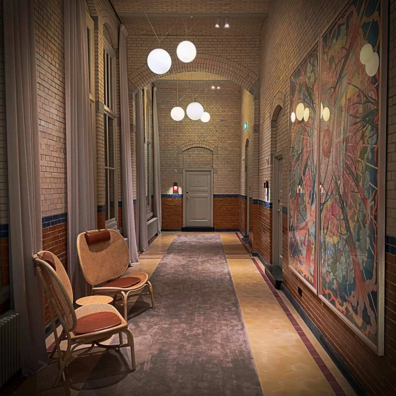 Moderner Hotelflur im Pillows Hotel Amsterdam mit historischen glasierten Ziegelwänden, zwei Sesseln und großen Wandgemälden.