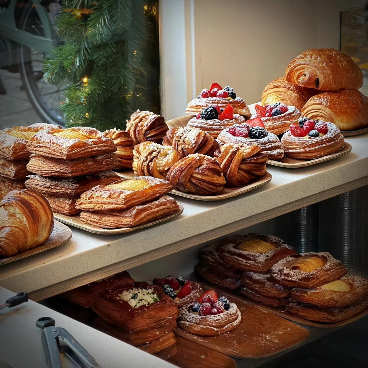 Auswahl an frischem Gebäck im Coffee District am Willemsparkweg in Amsterdam – Pain au Chocolat, Fruchttörtchen, Zimtknoten und Blätterteig mit Puderzucker.