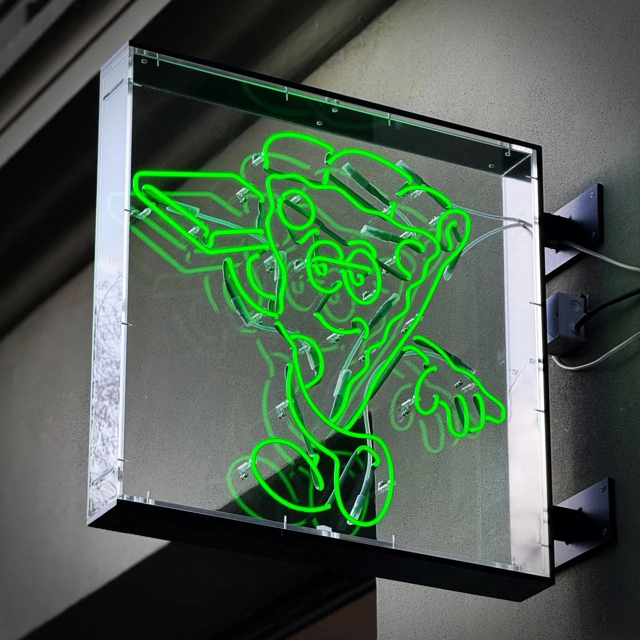 Green neon sign with a cartoon pizza slice mounted on a grey wall, photographed outside Slice Society in Berlin.
