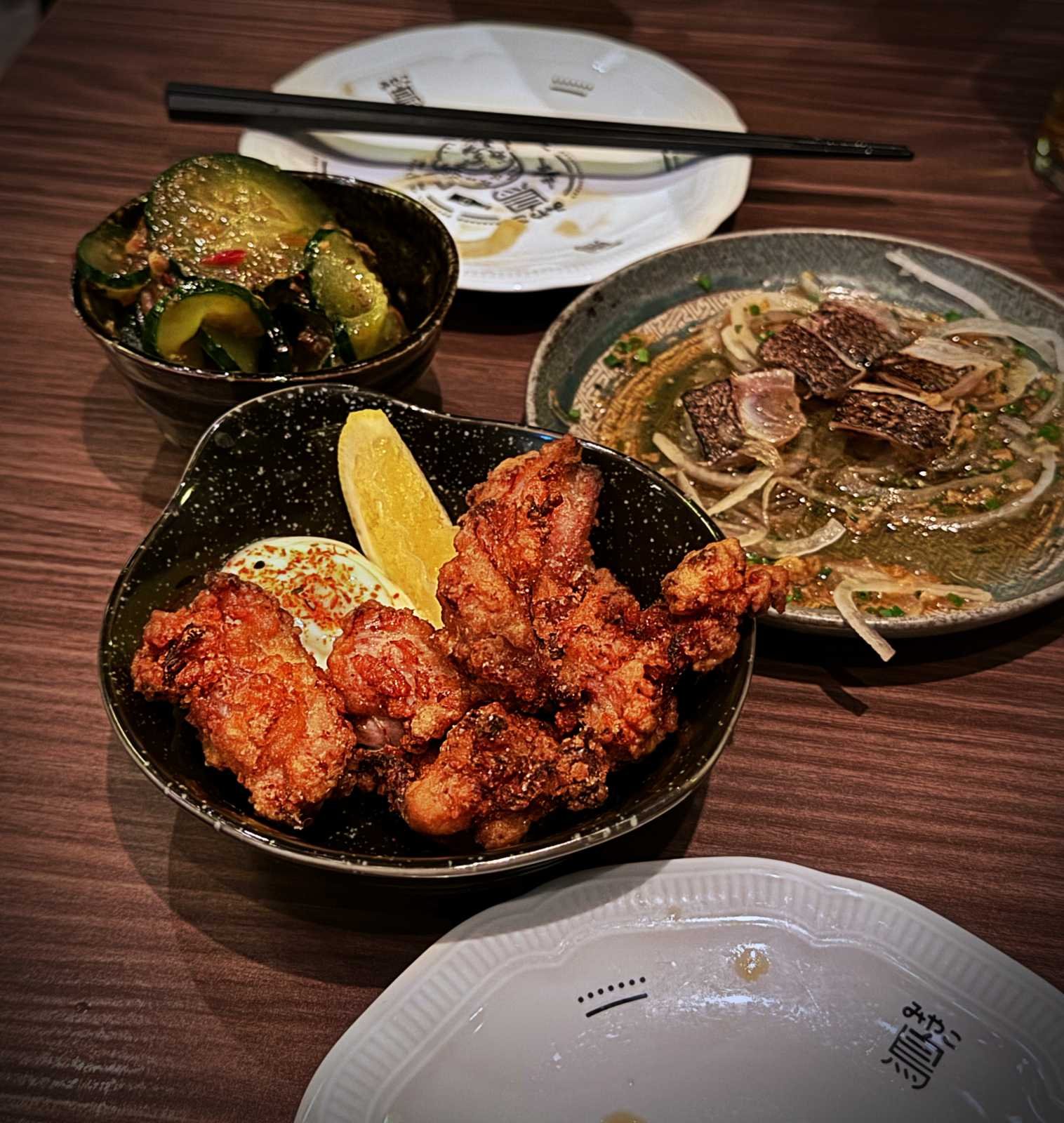 Japanese fried chicken (Karaage) with lemon, cucumber salad, and tataki fish on a dark wooden table at Miyakodori restaurant in Stockholm.