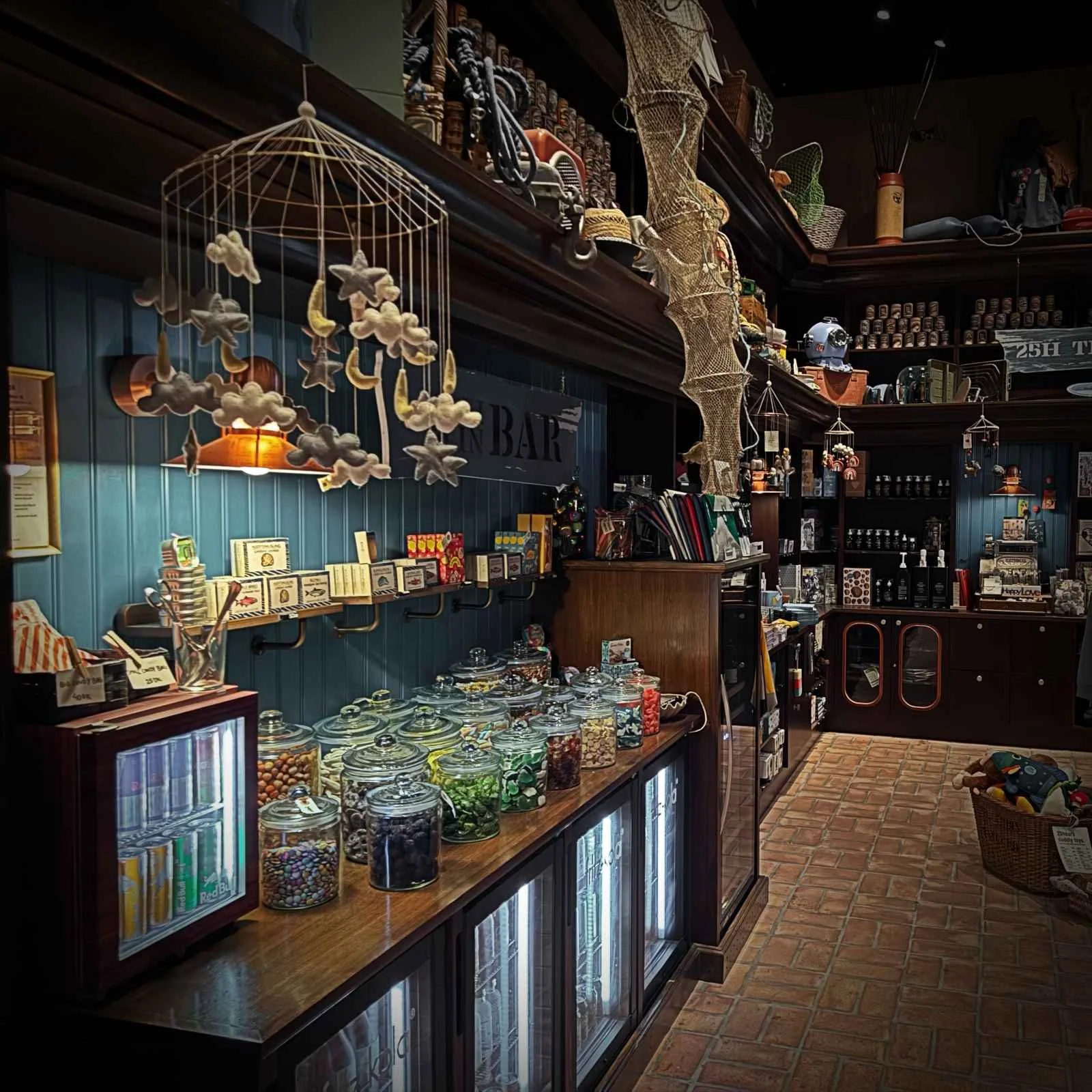 Blick auf Bonbongläser auf einem Holztresen im 25hours Hotel Paper Island. Über der Auslage hängt ein Mobile mit Stoffwolken vor einer blauen Wand mit Regalen und maritimer Deko.