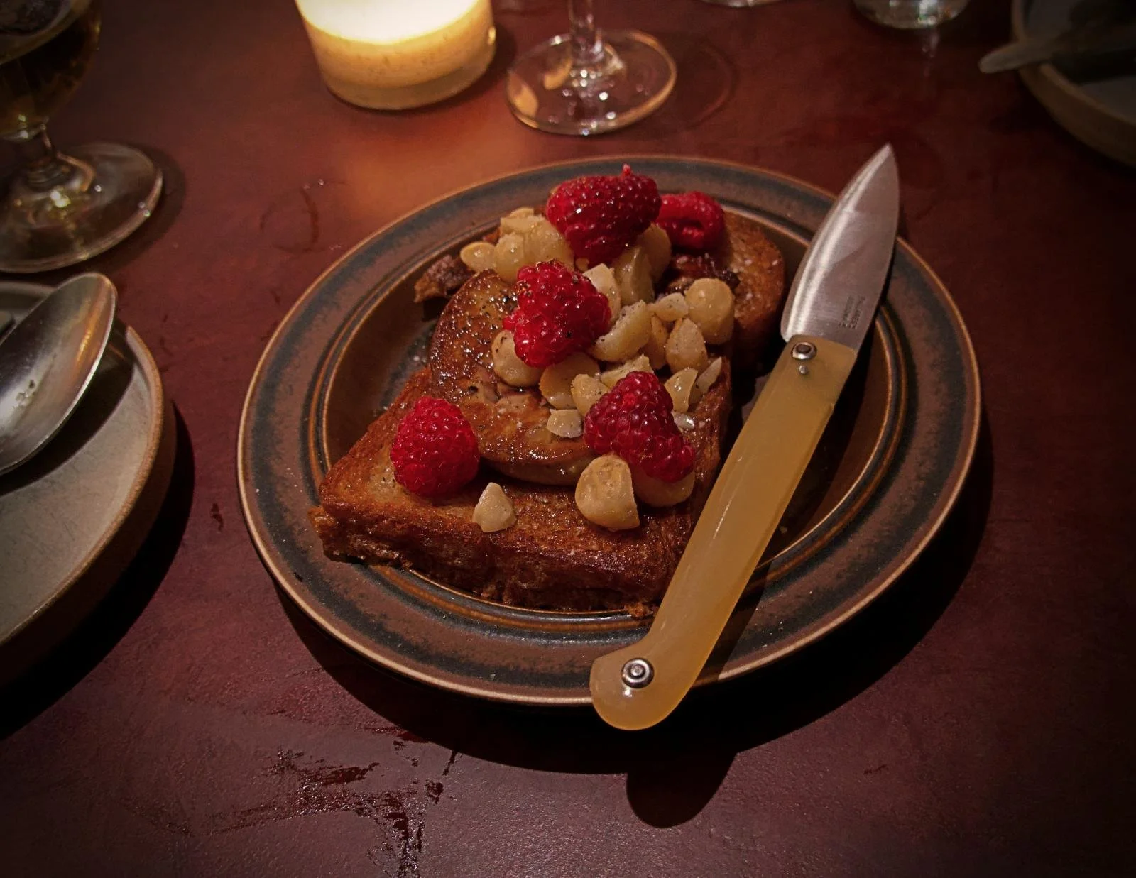 Nahaufnahme des Gerichts „Foie Gras, Brioche, Himbeeren, Macadamia und Ahornsirup“ auf einem rustikalen Teller im Restaurant Främmat in Stockholm.