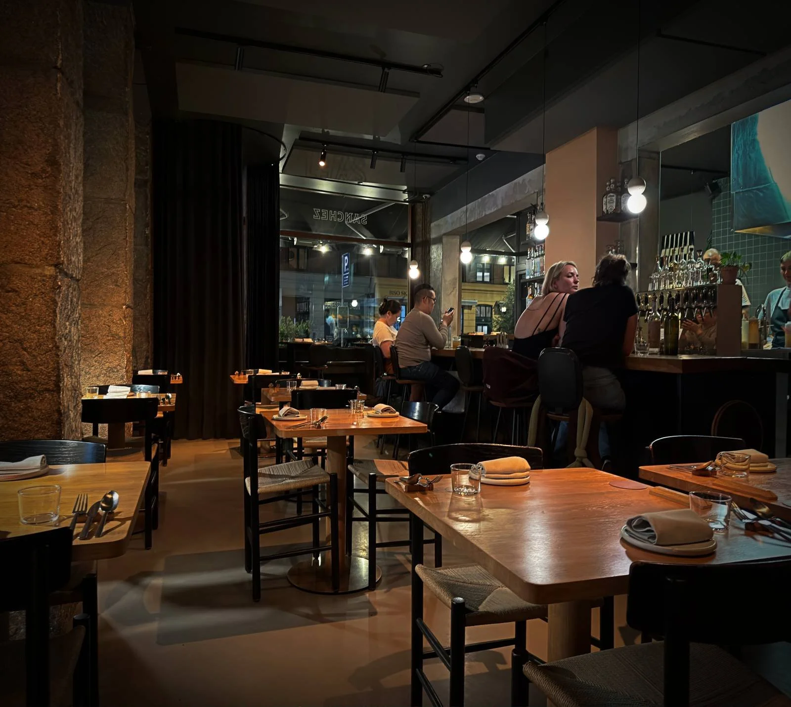 Der Gastraum des Restaurants Sanchez in Kopenhagen Vesterbro mit Holztischen, Gästen an der Bar und gemütlicher Abendbeleuchtung.