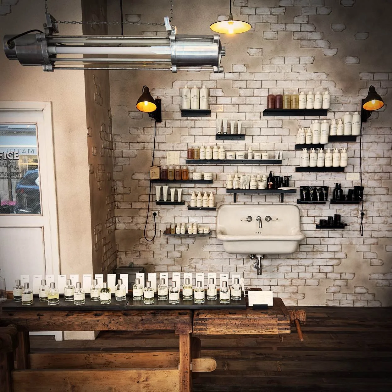 Der Innenraum der Parfümerie Le Labo in München mit Flakons auf Regalen, einem Waschbecken im Zentrum und Fliesenwänden.