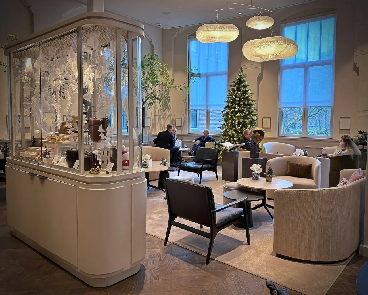 Elegante Lounge im Pillows Hotel Amsterdam mit gemütlichen Sesseln, festlichem Weihnachtsbaum und einer großen gläsernen Vitrine.
