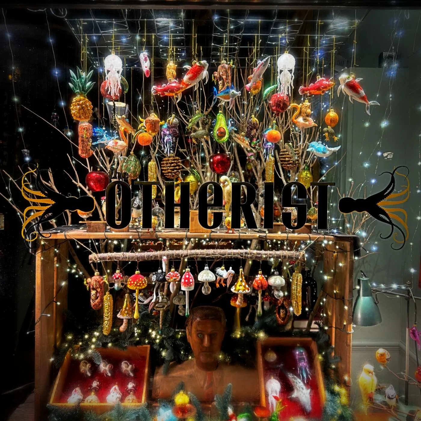 Das beleuchtete Schaufenster des Ladens „The Otherist“ in Amsterdam. Zahlreiche handgefertigte Christbaumkugeln in Form von Fischen, Pilzen und Tieren hängen an Zweigen zwischen Lichterketten.
