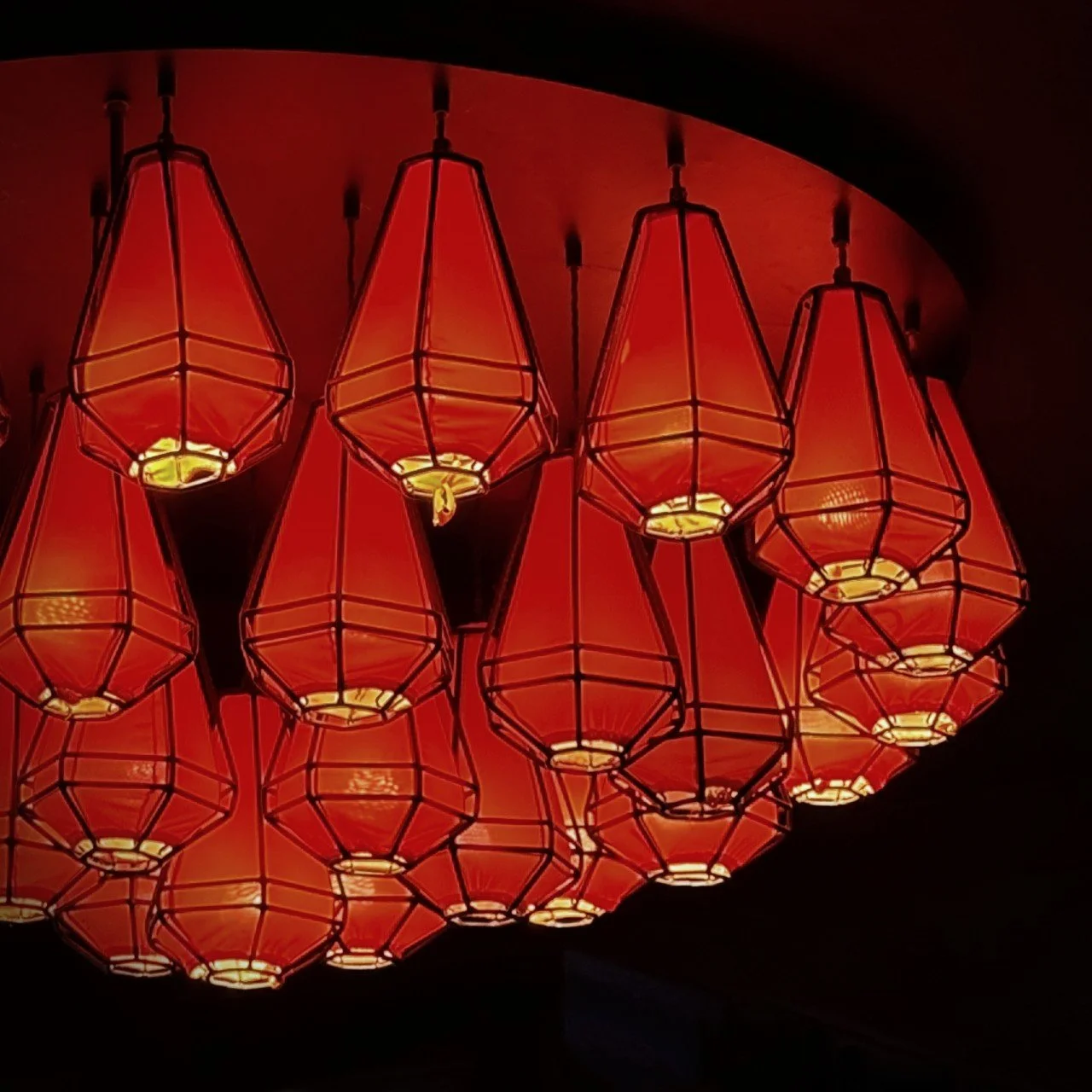 Mehrere rote Hängelampen in geometrischer Laternenform, gruppiert unter einer runden Decke im Innenraum eines asiatischen Restaurants.