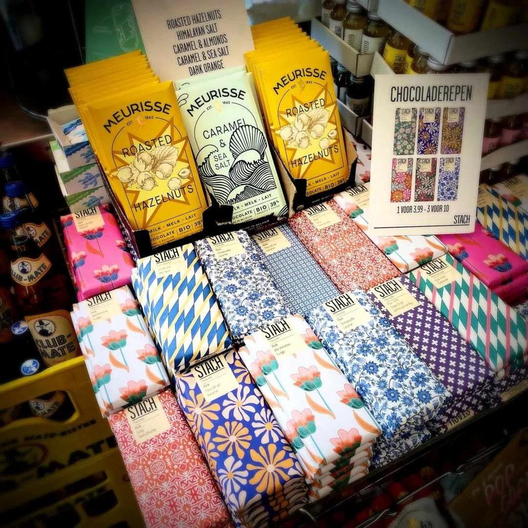 Colorful chocolate bars with floral patterns at Stach Food Amsterdam, alongside flavors like caramel & sea salt.
