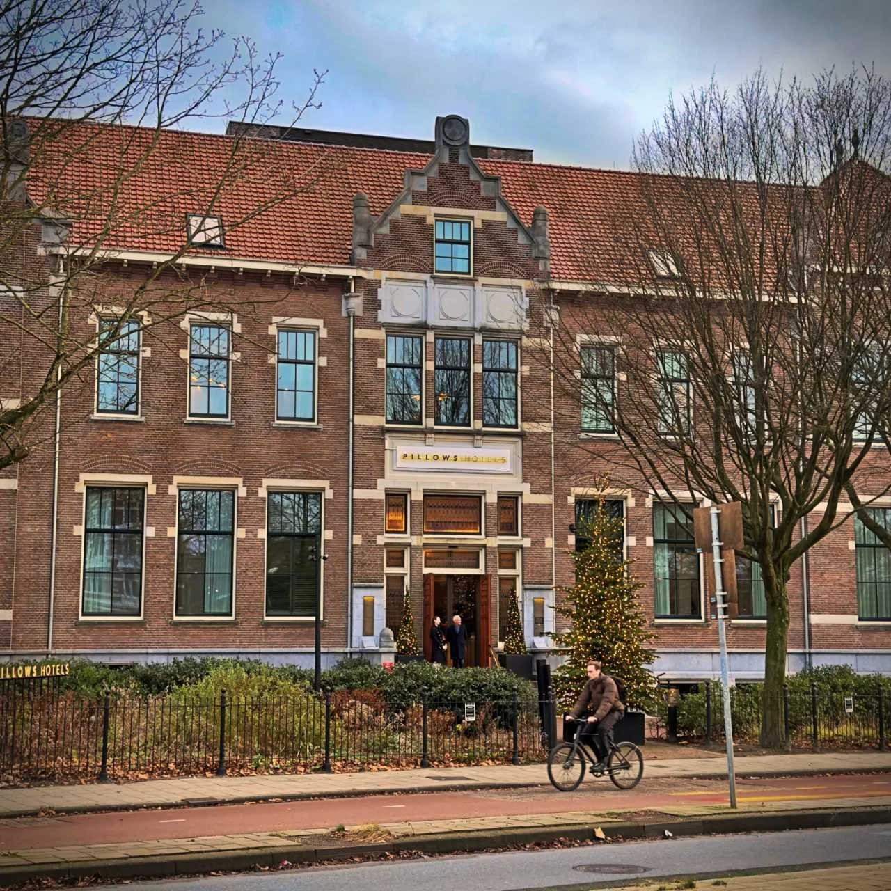 Historische Backsteinfassade des Pillows Hotels in Amsterdam mit festlichem Weihnachtsbaum und einem Radfahrer im Vordergrund.