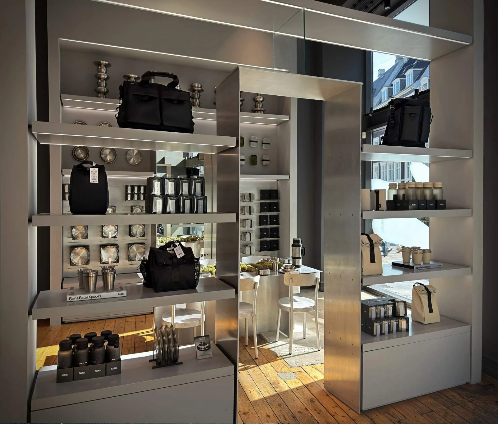 Ein helles Metallregal im Geschäft mit schwarzen Taschen, Trinkflaschen, Bechern und Edelstahl-Dosen.