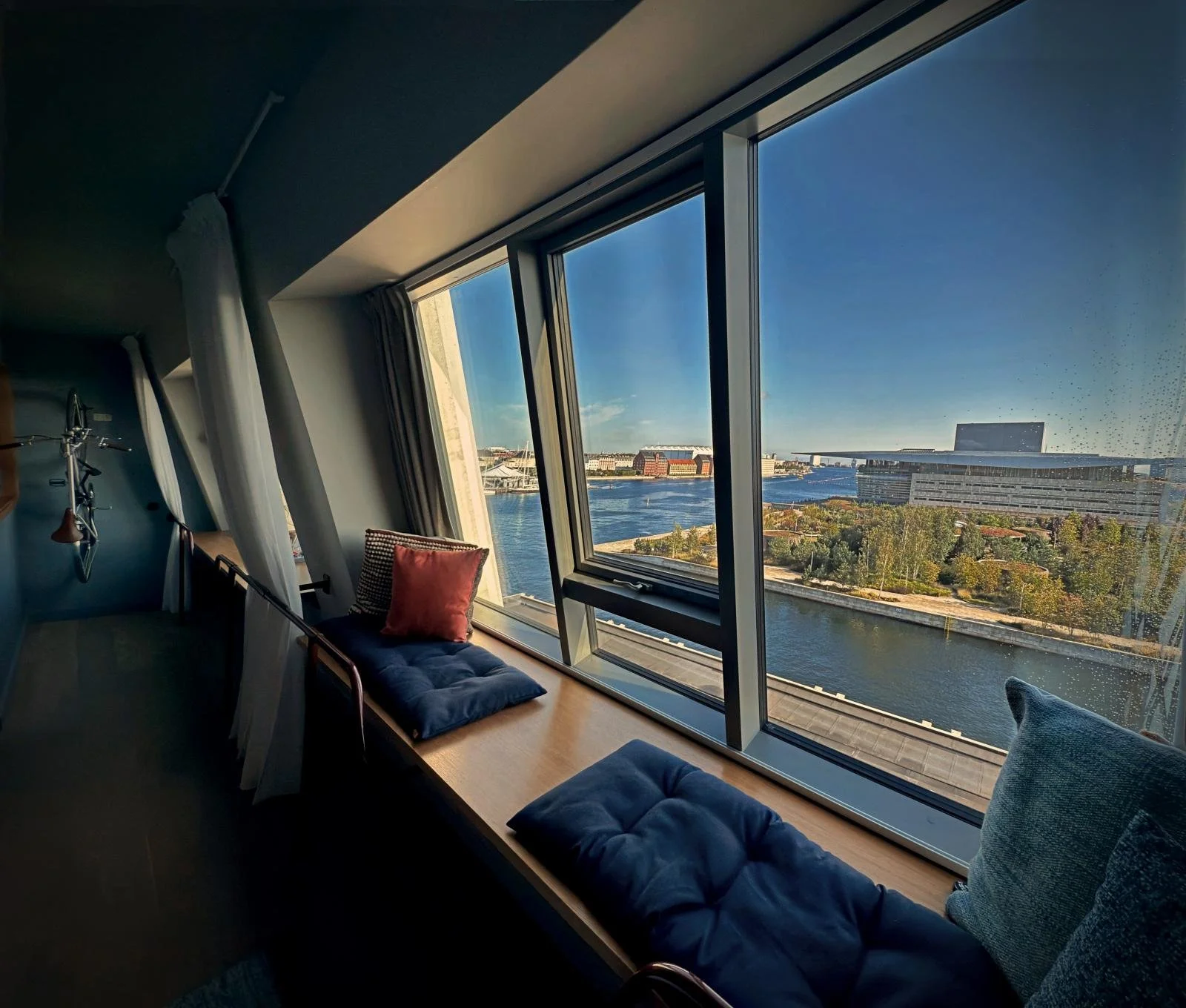 Sitzbank am Fenster mit Kissen und Ausblick auf das Opernhaus und den Hafen von Kopenhagen im 25 Hours Hotel Paper Island.