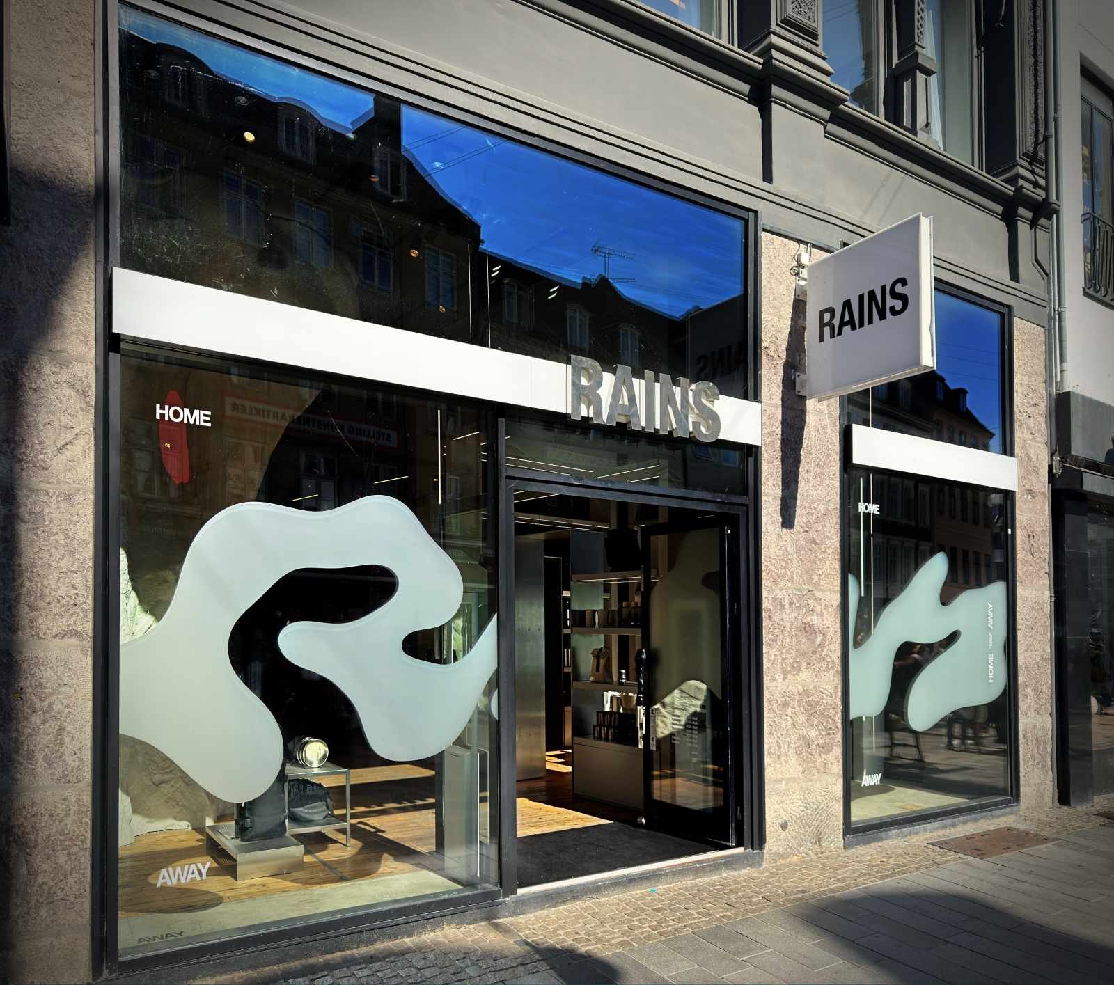 Schaufensterfront des Rains Flagship Stores mit Marken-Schriftzug und matten Folienmotiven auf den Scheiben.