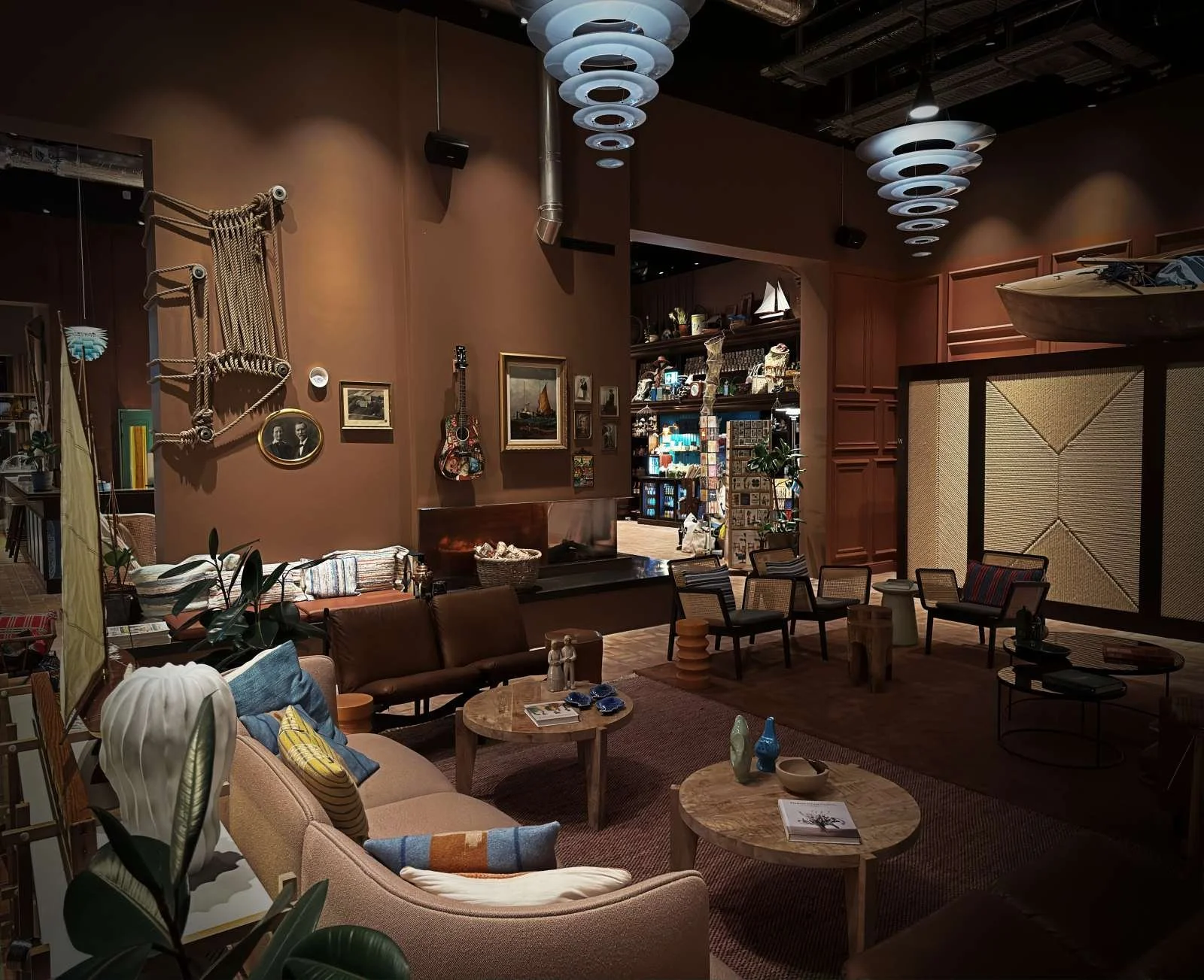 Kopenhagen: Lobby des 25hours Hotel Paper Island mit Sofas, Holztischen und Sesseln vor braunen Wänden. Nautische Dekorelemente wie Seile und Bilder ergänzen die runden Hängelampen an der Decke.