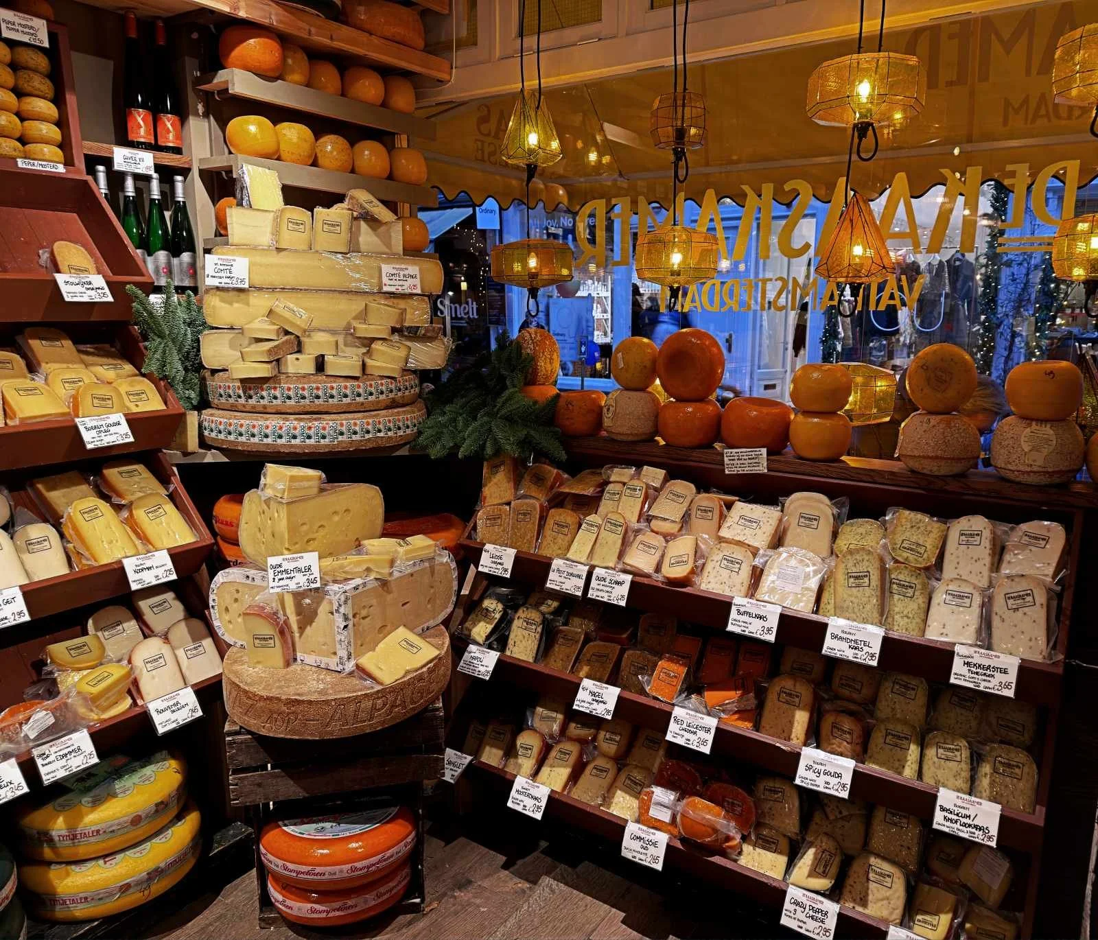 Der Verkaufsraum von De Kaaskamer in Amsterdam zeigt Regale voller Käse. Verschiedene Sorten sind mit Preisschildern versehen. Gelbe Hängelampen beleuchten die Auslage im Geschäft.