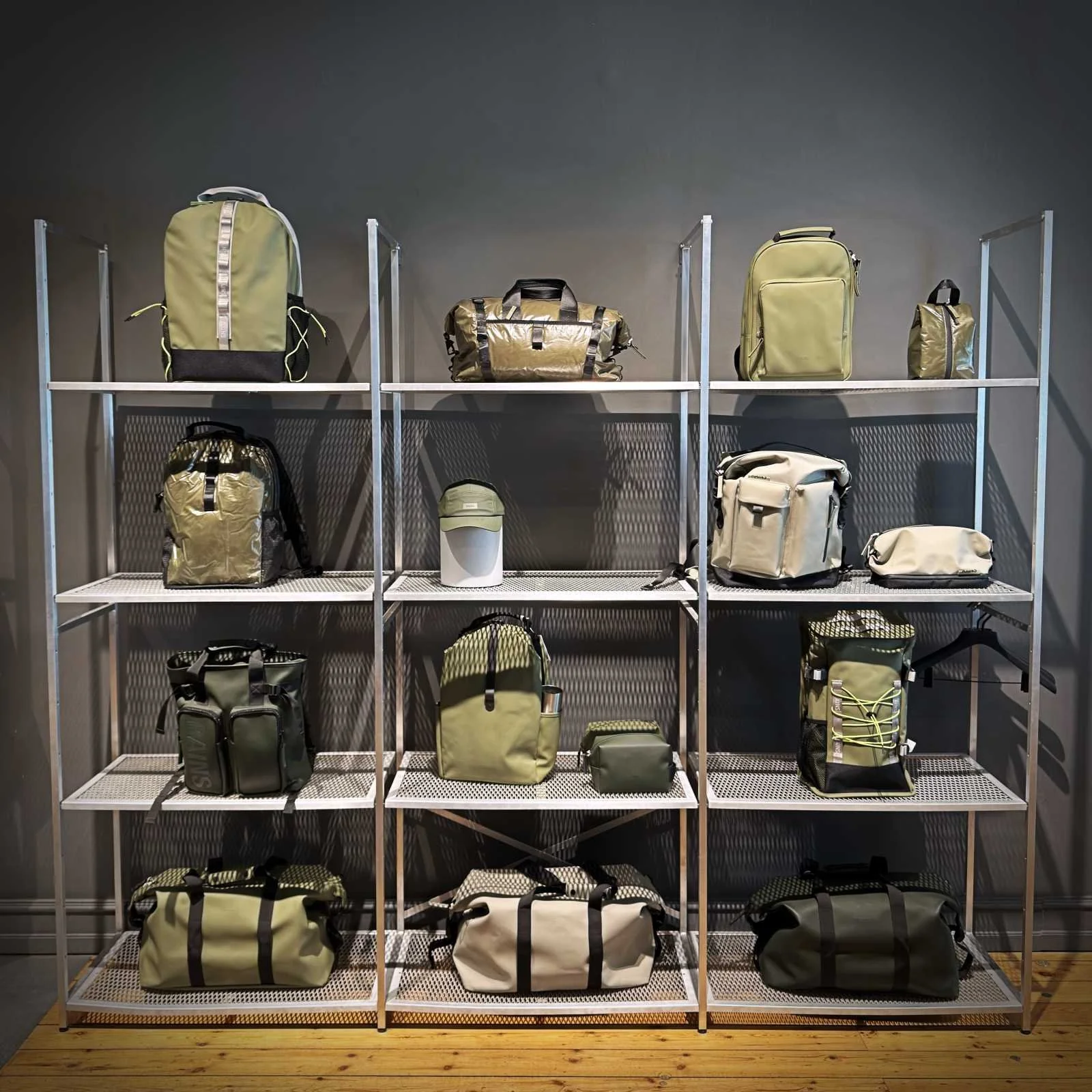 Ein Metallregal im Rains Store, auf dem verschiedene olivgrüne Rucksäcke, Reisetaschen und Accessoires ausgestellt sind.