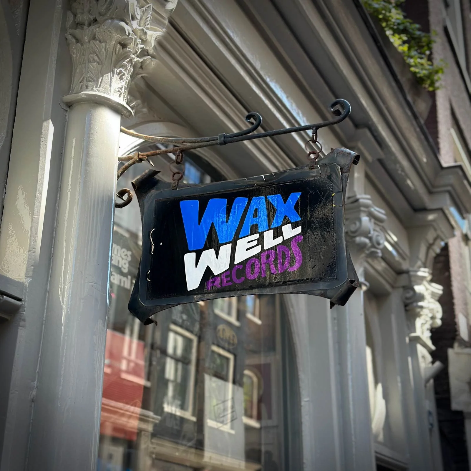 A sign saying "Wax Well Records" hangs in front of a record store. The logo is in blue, white, and purple.