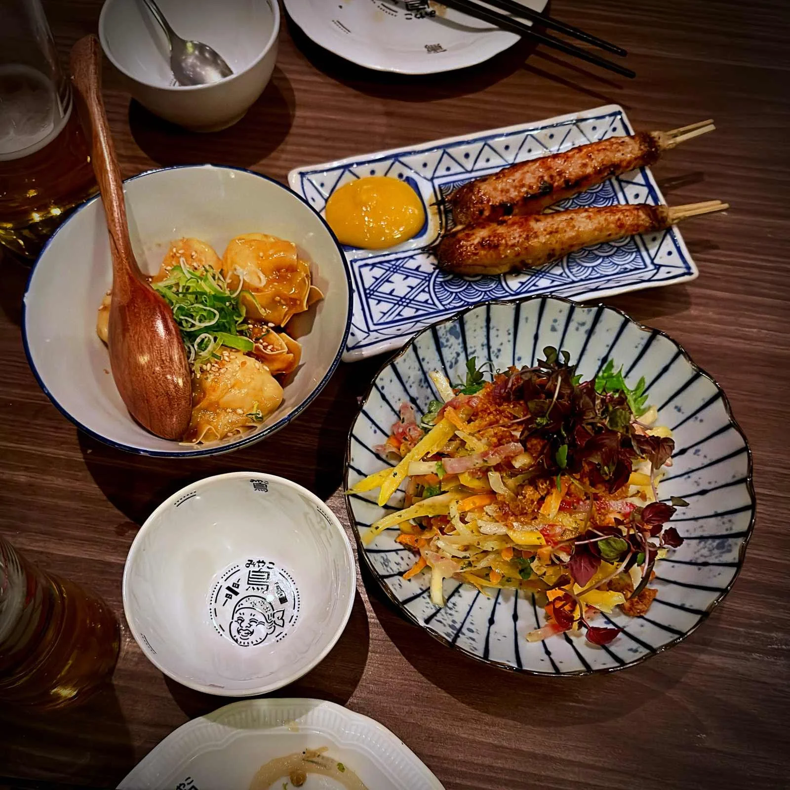 Japanese dishes at Miyakodori restaurant in Stockholm featuring grilled skewers, dumplings, and a salad on a dark wooden table.