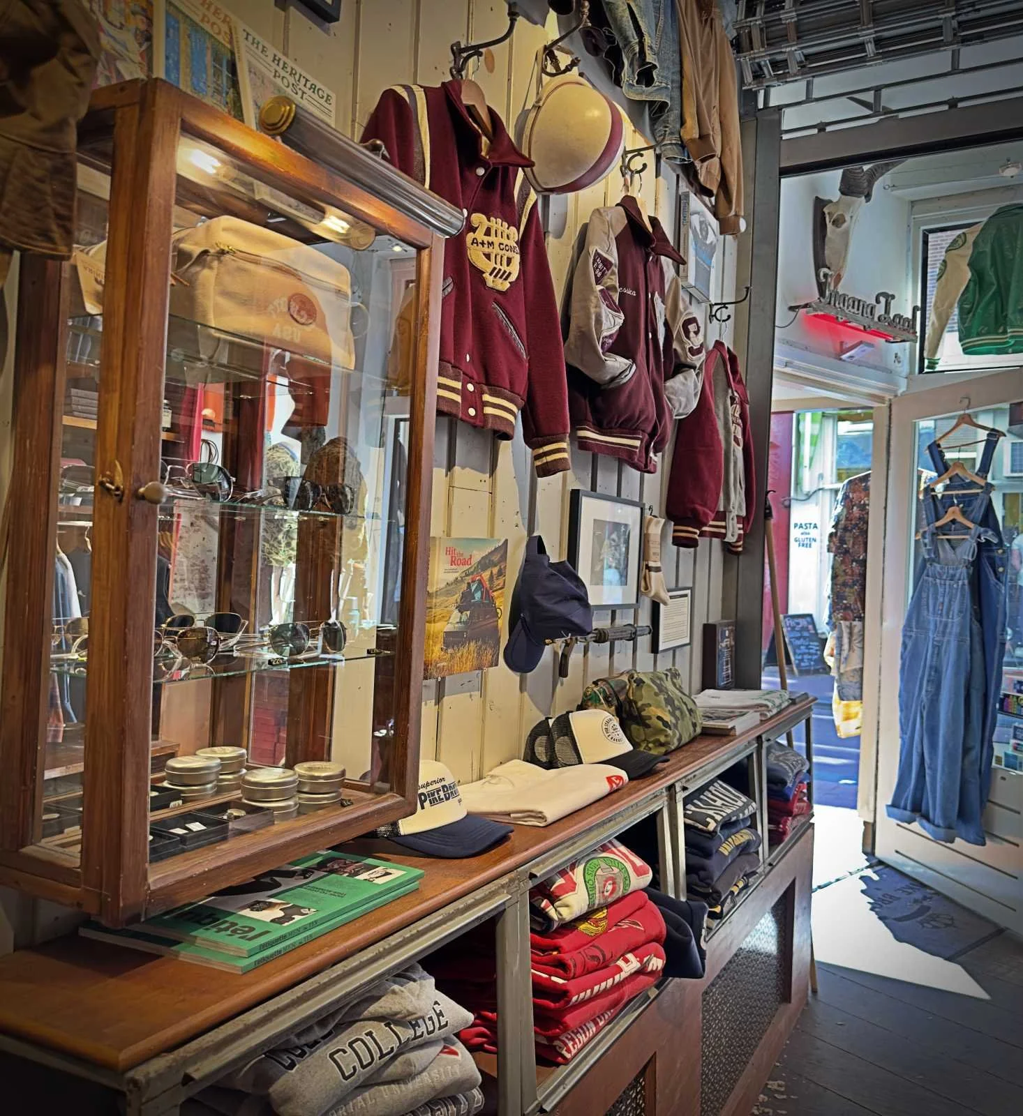 Inside Concrete Matter: Varsity jackets hang on the wall of the vintage shop. Sunglasses are displayed in a glass case, with piles of clothes on the shelves below.