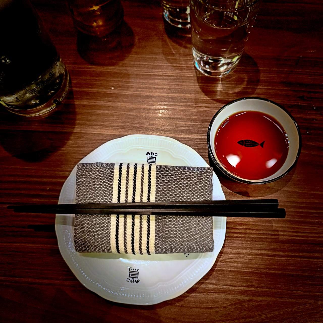 Table setting at Miyakodori restaurant in Stockholm featuring a plate, cloth napkin, chopsticks, and a soy sauce bowl on a wooden table.