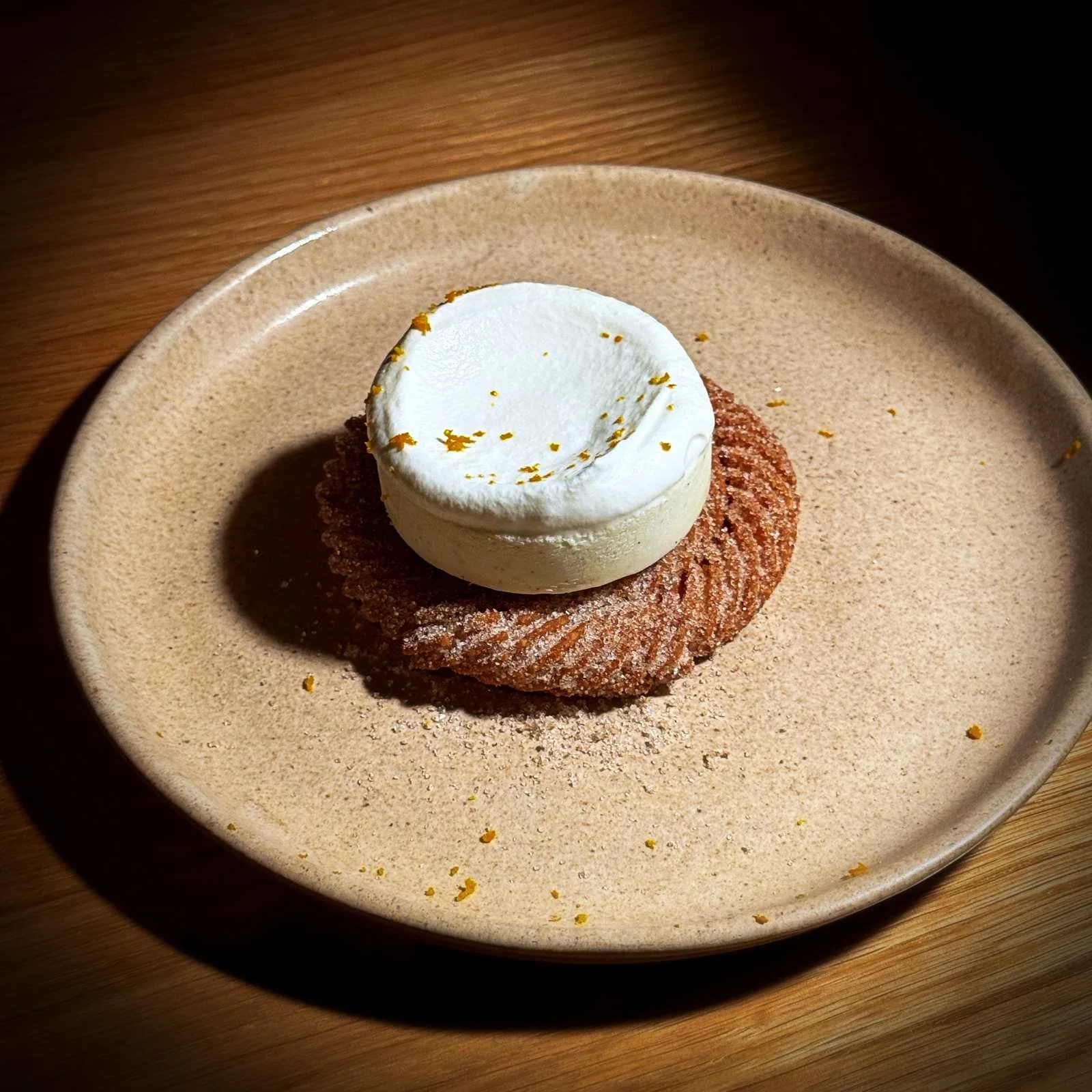 Ein rundes Churro-Sandwich mit einer Kugel Eiscreme und Orangenabrieb auf einem Teller im Restaurant Sanchez in Kopenhagen Vesterbro.