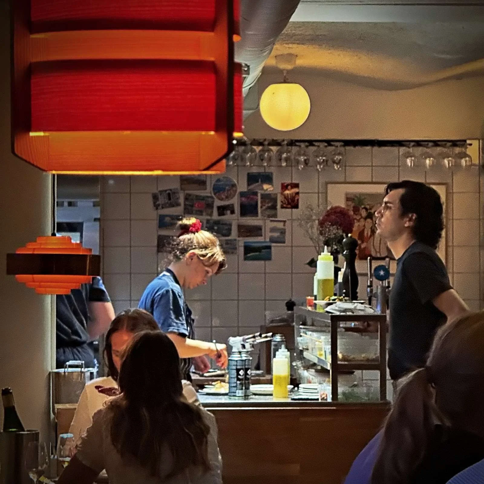 Blick auf das geschäftige Treiben im Restaurant Främmat in Stockholm, mit einer Köchin bei der Speisenzubereitung und Gästen im Vordergrund.