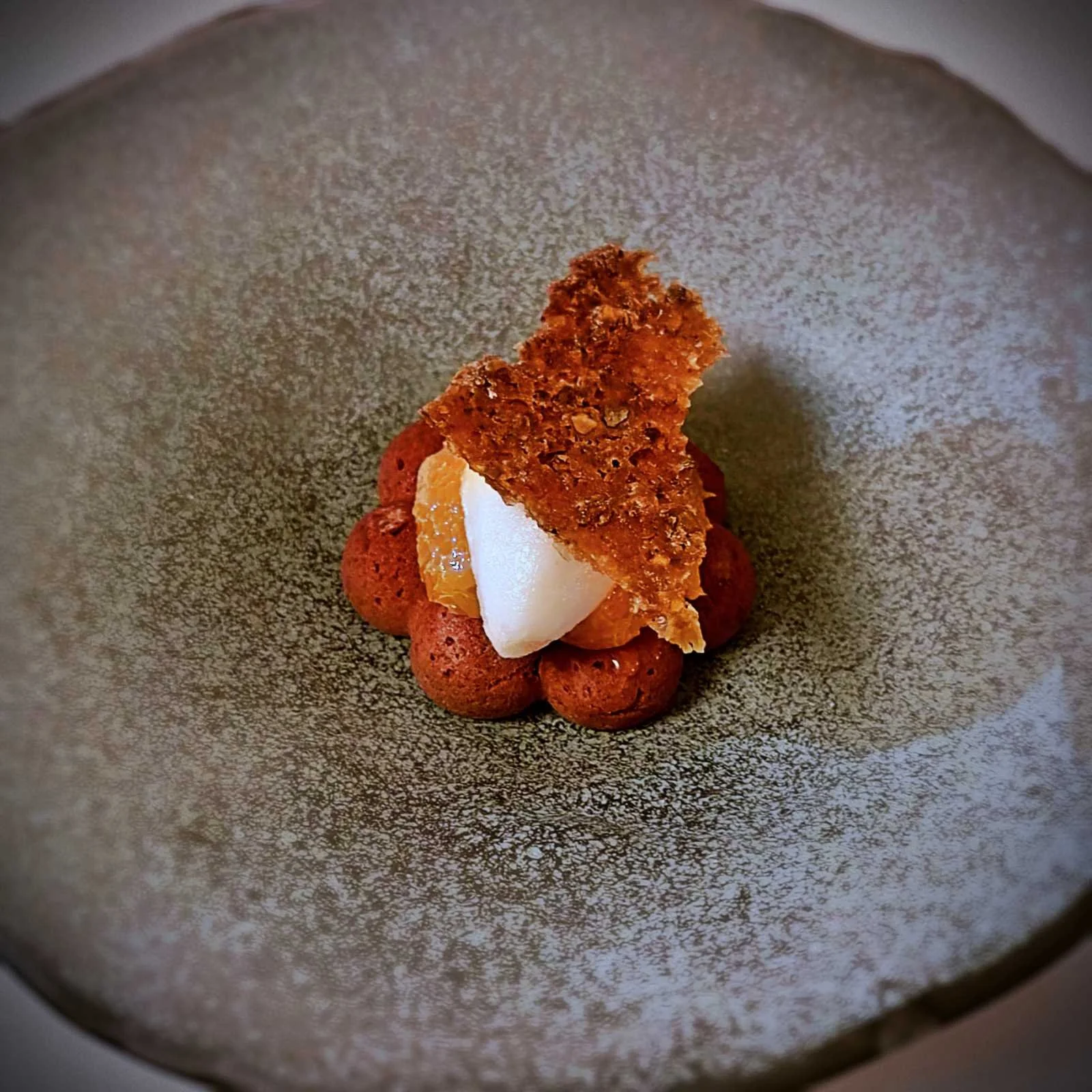 Das Dessert im Restaurant R21 in Amsterdam besteht aus einer dunklen Mousse-Basis, einem weißen Sorbet und einem knusprigen Keks. Es wird in einer grauen, gesprenkelten Schüssel serviert.