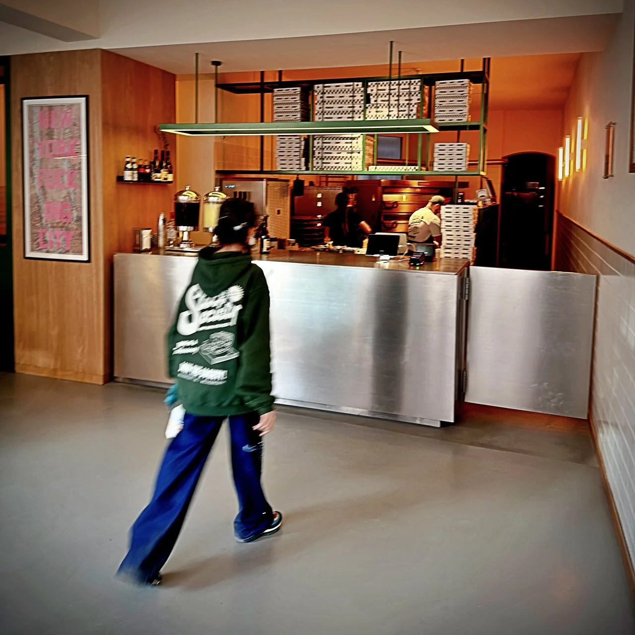 View of the open counter at Slice Society in Berlin with stacked pizza boxes, two staff members in the back and a person walking past in the foreground.