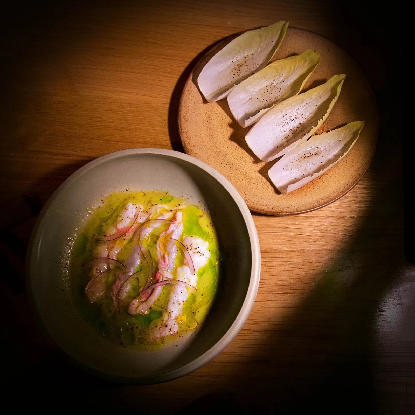 Langustino Ceviche mit roten Zwiebeln und Chicorée-Blättern serviert auf einem Holztisch im Restaurant Sanchez in Kopenhagen Vesterbro.