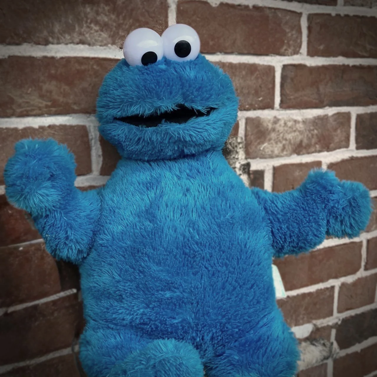 Ein blaues Krümelmonster-Plüschtier lehnt an einer Ziegelwand – das Maskottchen des Cookie-Shops Krümel in Stockholm.