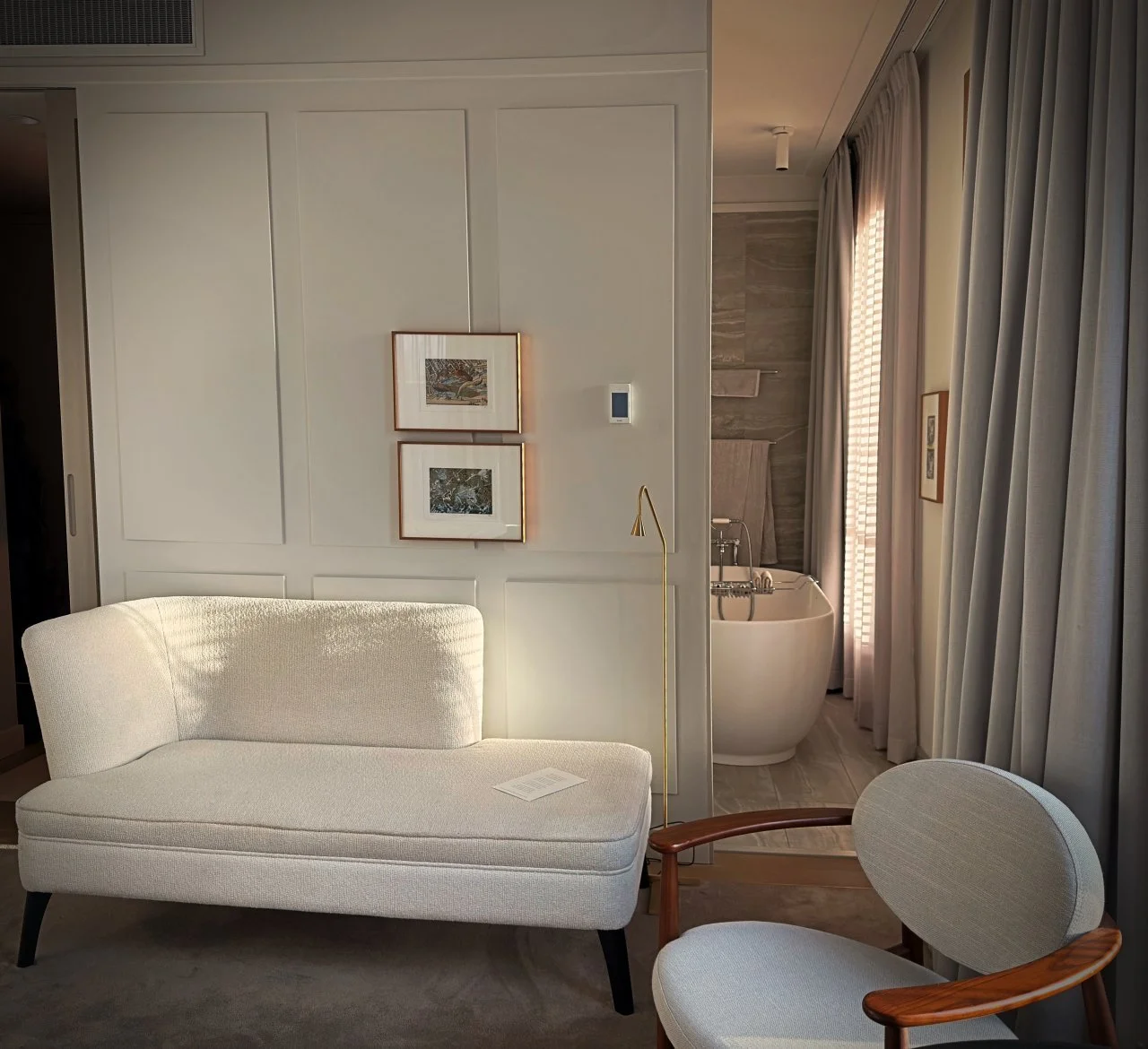 Hellgraue Récamiere und ein Sessel mit Holzlehnen vor einer weißen Wandpaneele in einer Suite des Pillows Hotels in Amsterdam.