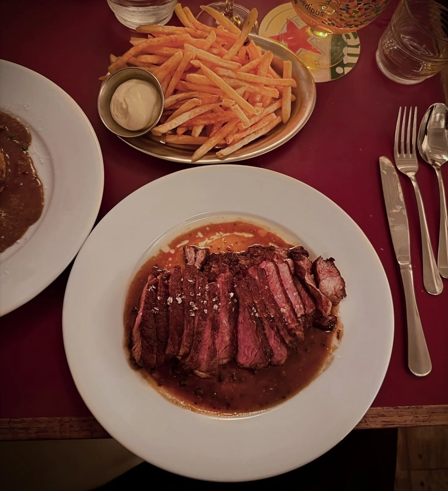 The sliced ribeye steak rests in dark pepper sauce on the plate. Beside it stands a portion of thin, crispy french fries.