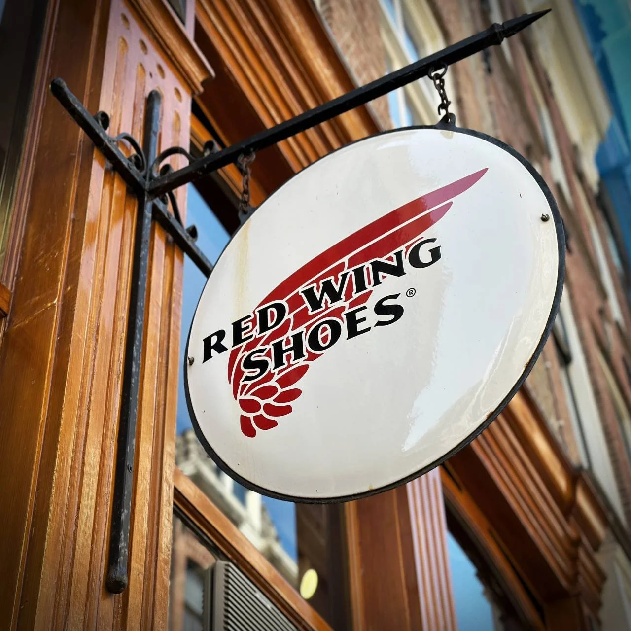 Ein rundes Schild mit dem Logo von Red Wing Shoes hängt an einer Metallhalterung über dem Eingang. Der Laden befindet sich in einer der Gassen der Neun Straßen.