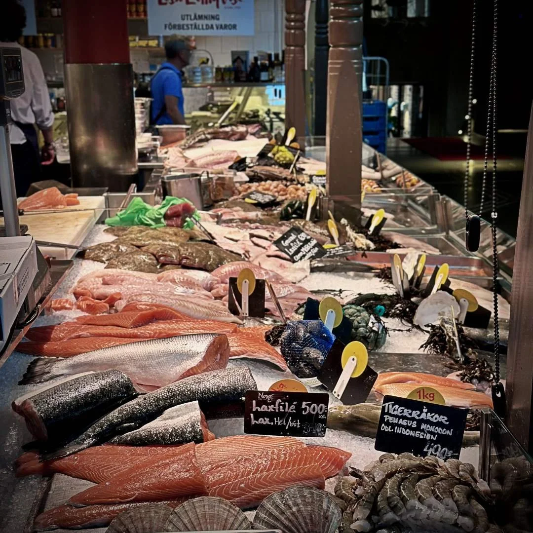 Eine große Auswahl an frischem Fisch und Meeresfrüchten liegt auf Eis in der Östermalms Saluhall. Zu sehen sind unter anderem Lachsfilets, Tigergarnelen und Jakobsmuscheln mit handbeschriebenen Preisschildern.
