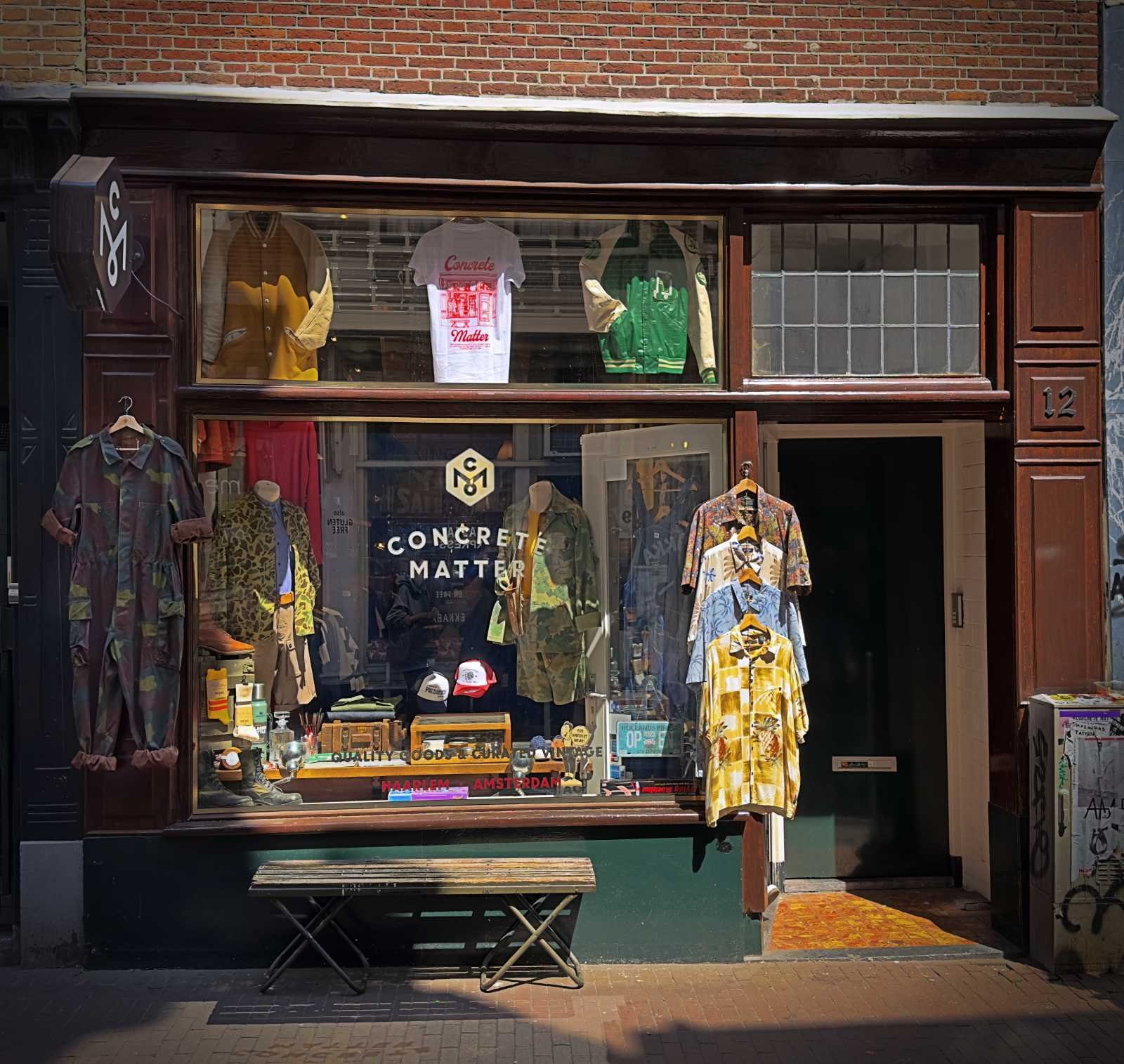 Exterior view of the Concrete Matter shop in the Nine Streets. Vintage jackets and shirts hang in the display window, with a camouflage suit attached to the facade on the left.
