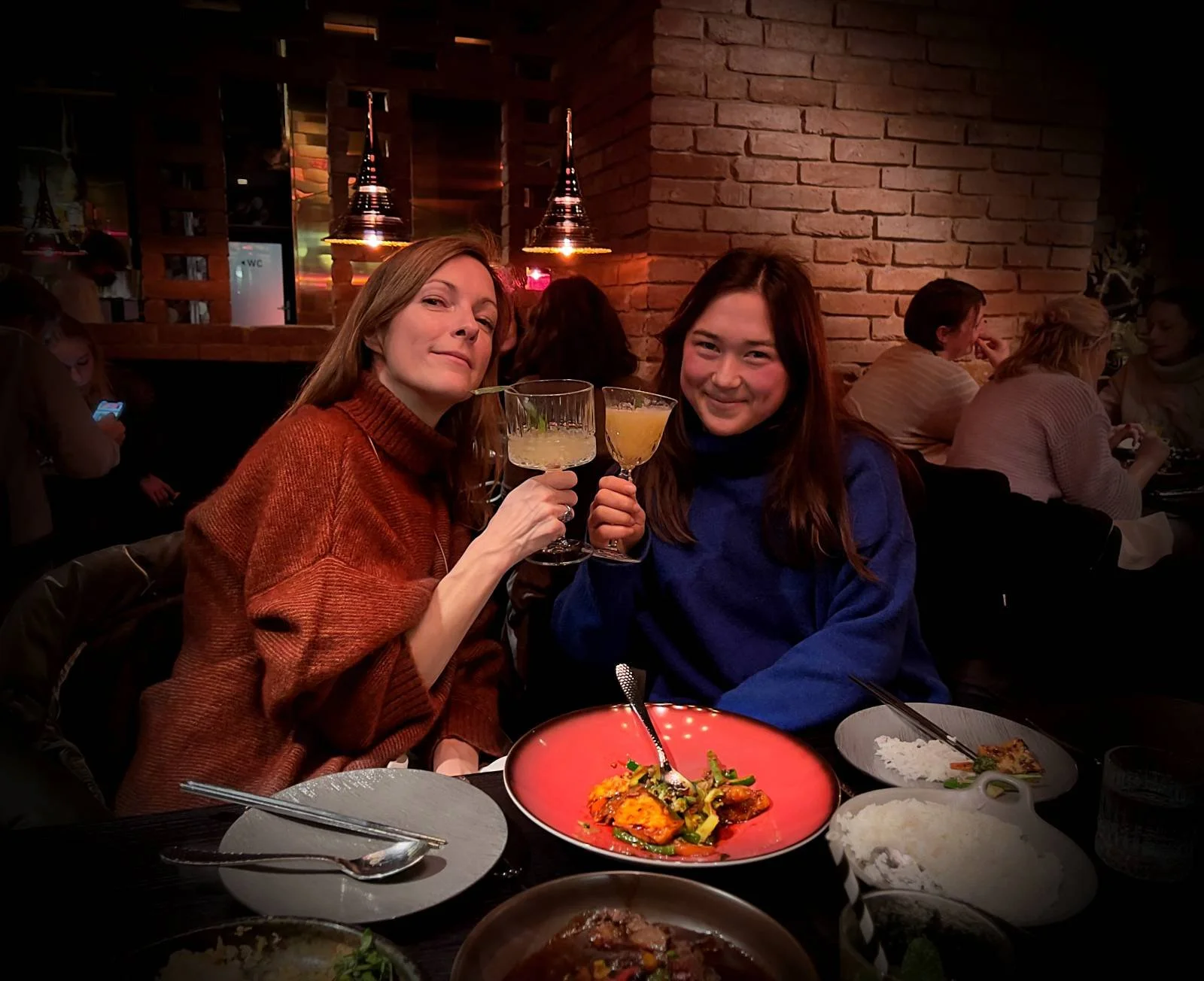 Zwei Gläser mit Cocktails und Garnitur stehen auf einem dunklen Holztisch im Innenraum des südostasiatischen Restaurants Aimy in München. Im Hintergrund sind gedimmte Lichter und Holzelemente erkennbar.