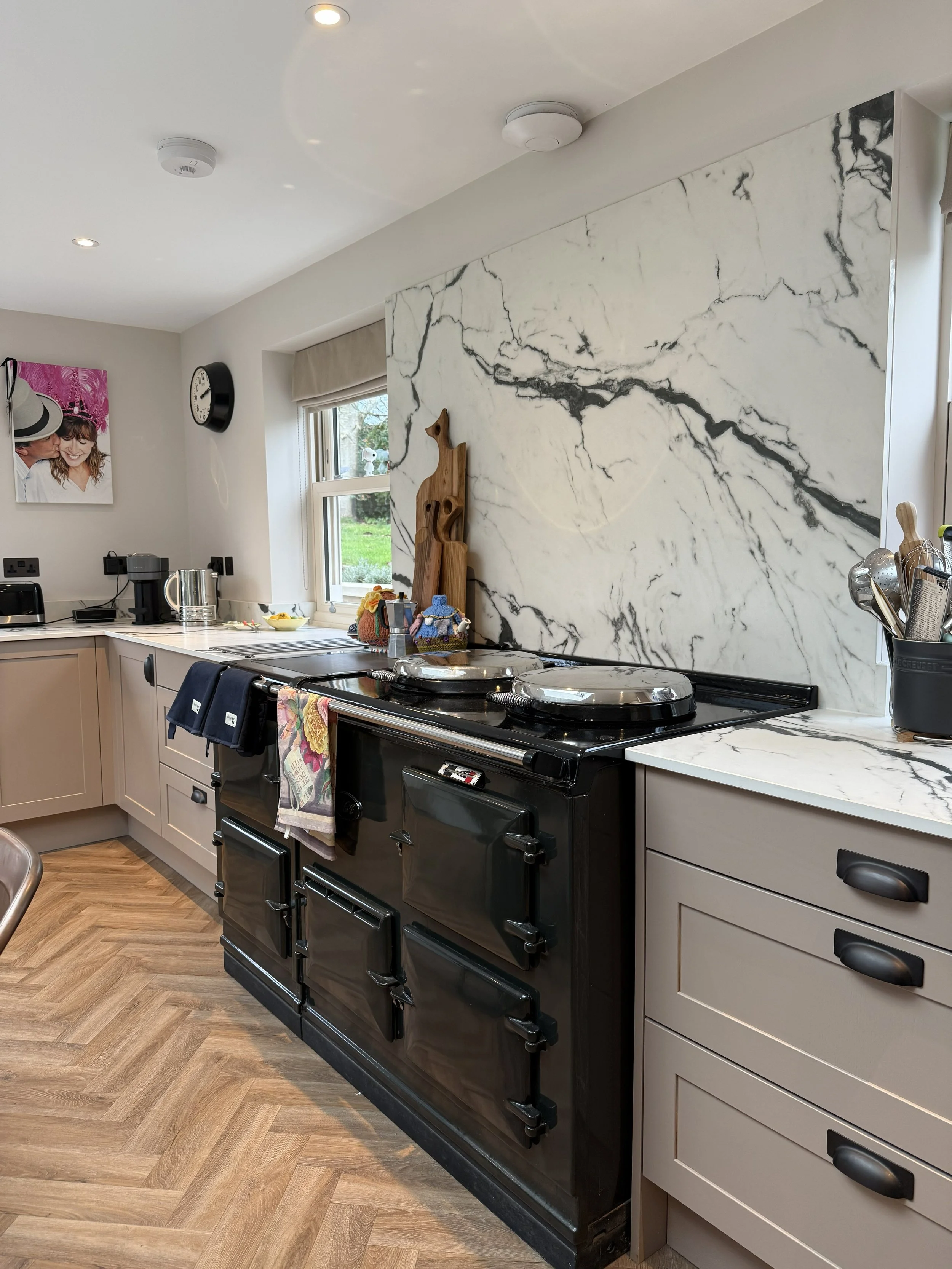 Kitchen with black stove, beige cabinets, marble backsplash, window, and decorative wooden giraffe on the counter.