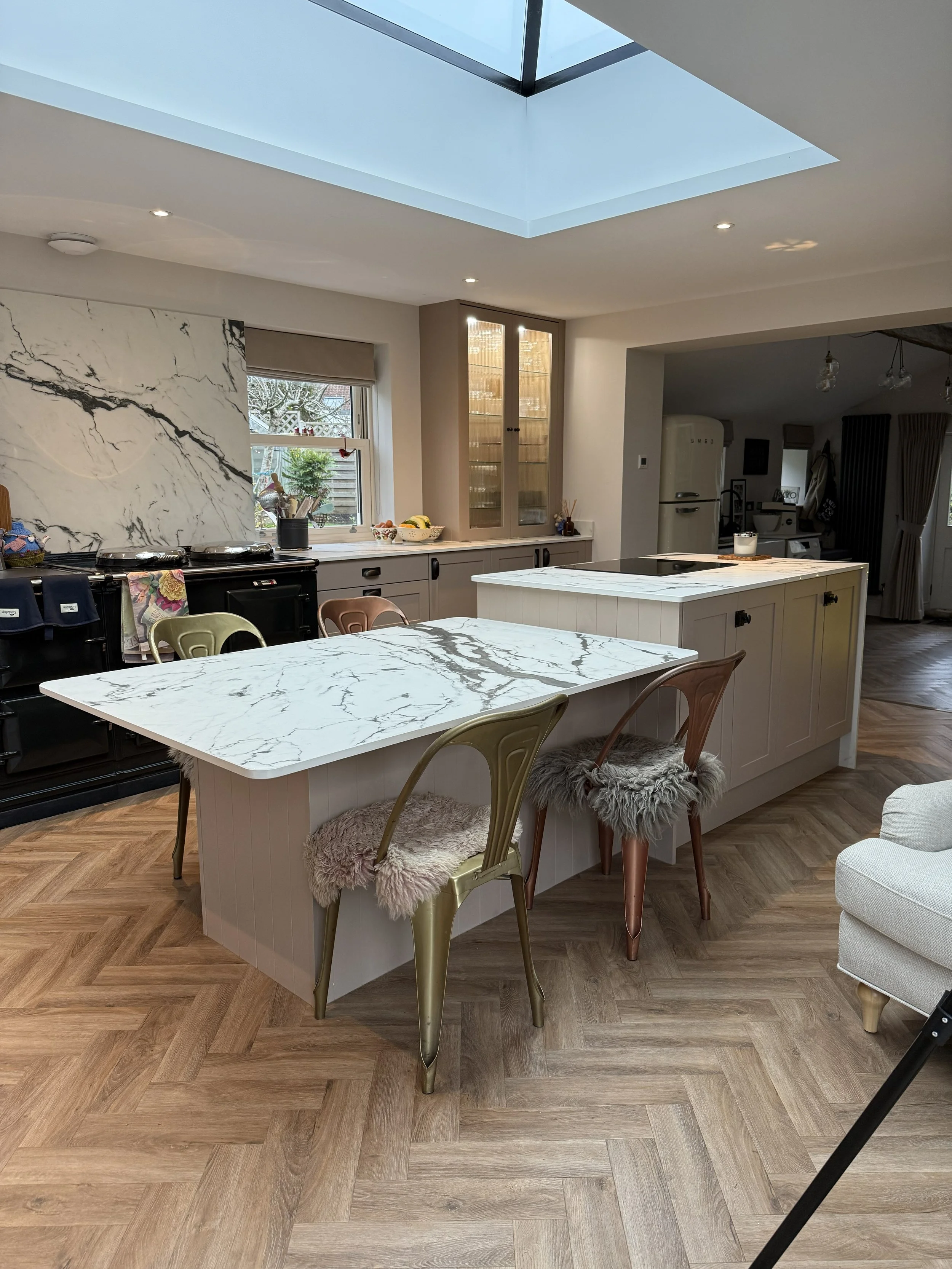 Modern kitchen with marble-topped island, wooden flooring, and a skylight ceiling.