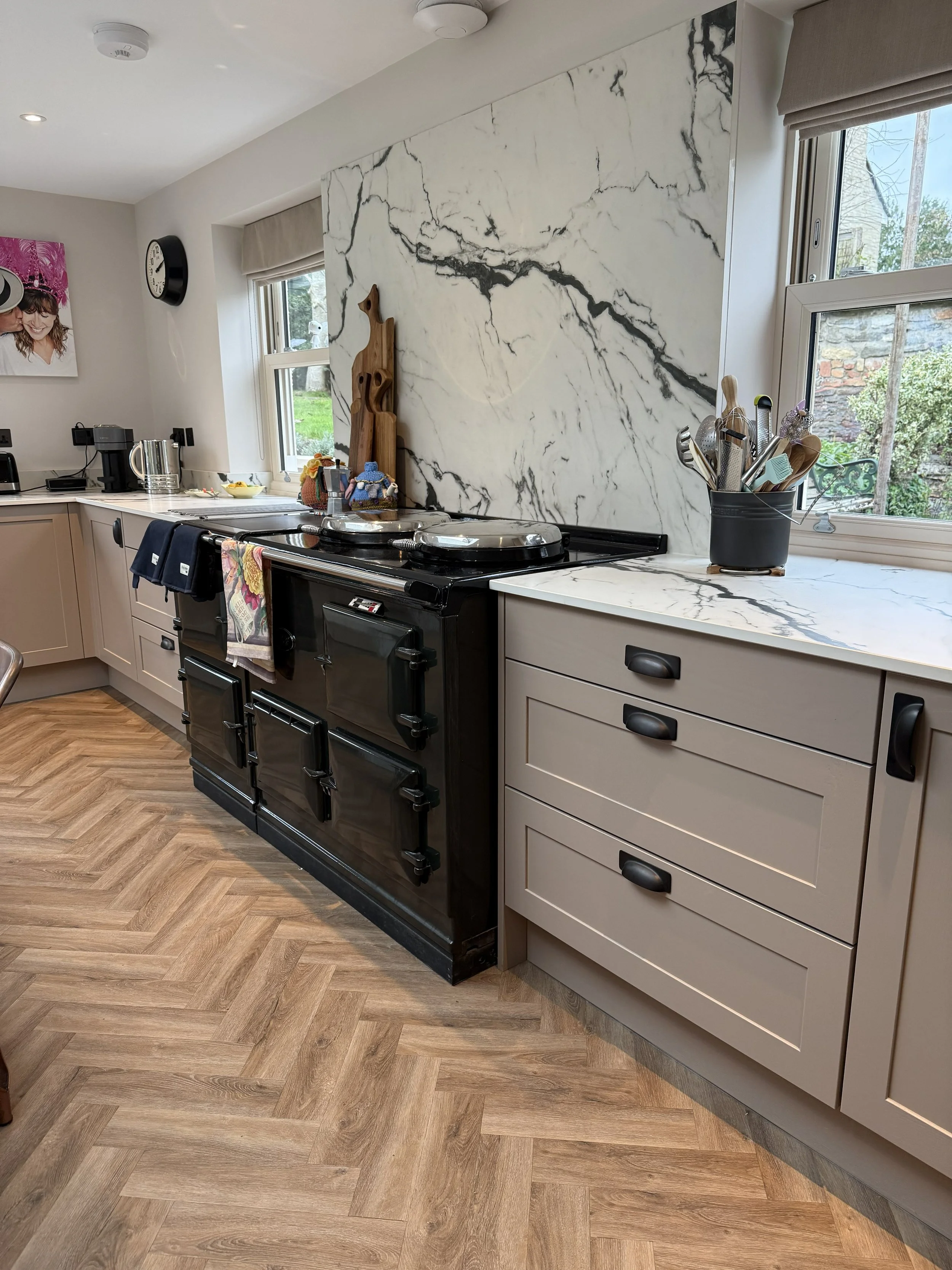 Modern kitchen with a black vintage stove, beige cabinets, marble backsplash, and herringbone wood flooring.