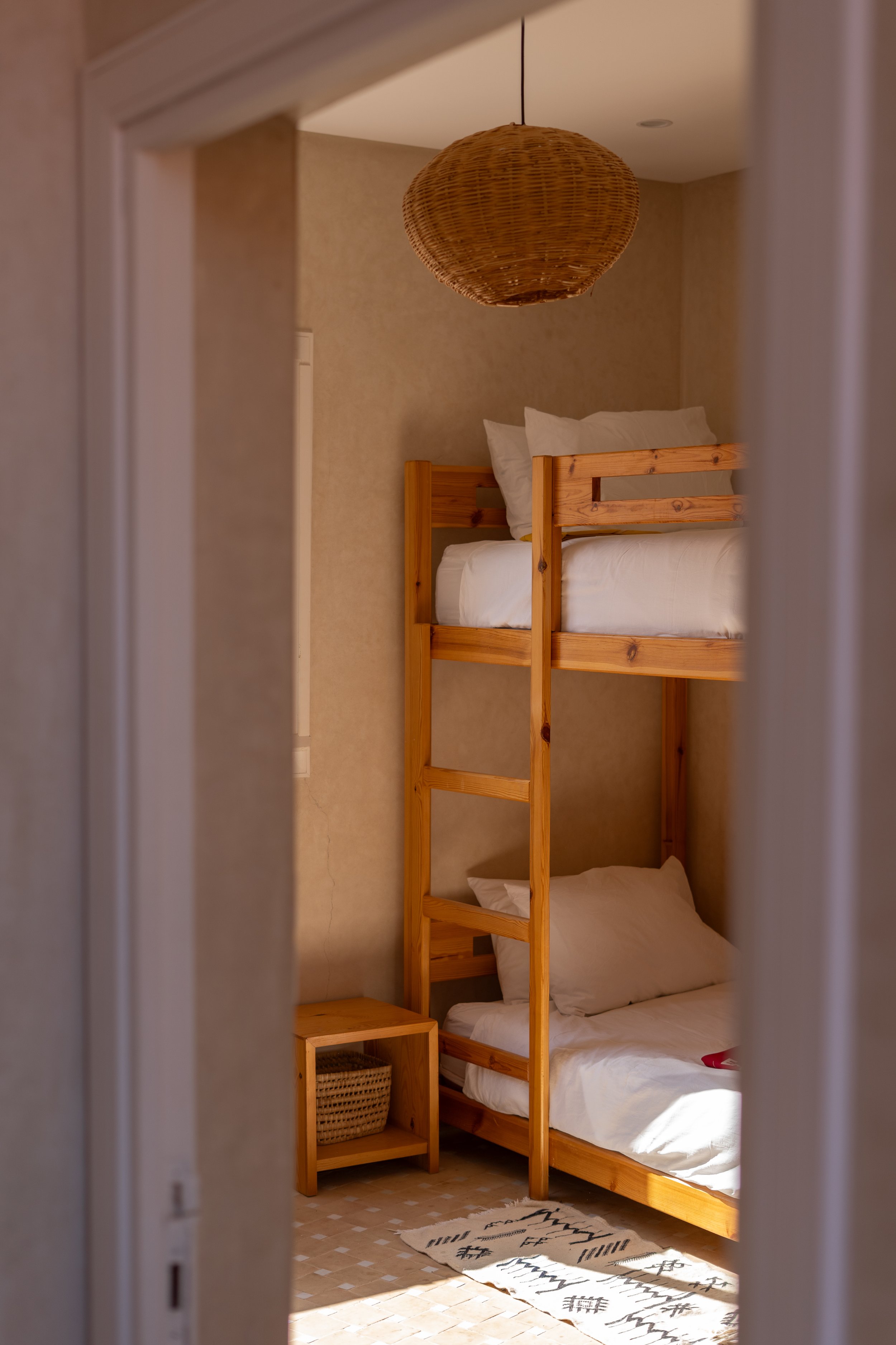 Chambre avec un lit en mezzanine en bois, dans une pièce éclairée par la lumière naturelle, avec un tapis blanc à motifs noirs