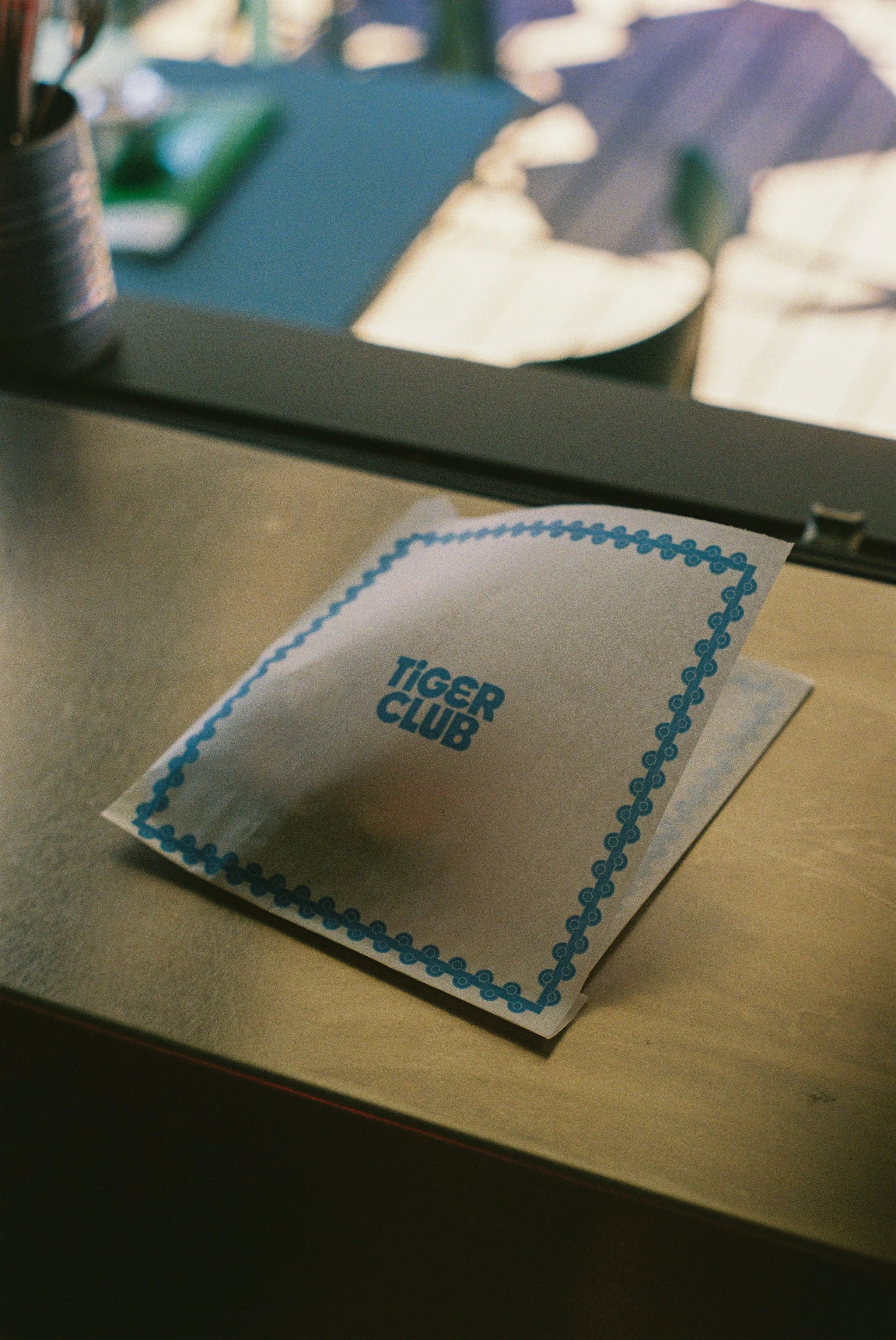 Un papier avec le logo 'Tiger Club' placé sur une surface à proximité d'une fenêtre, avec des objets flous en arrière-plan.