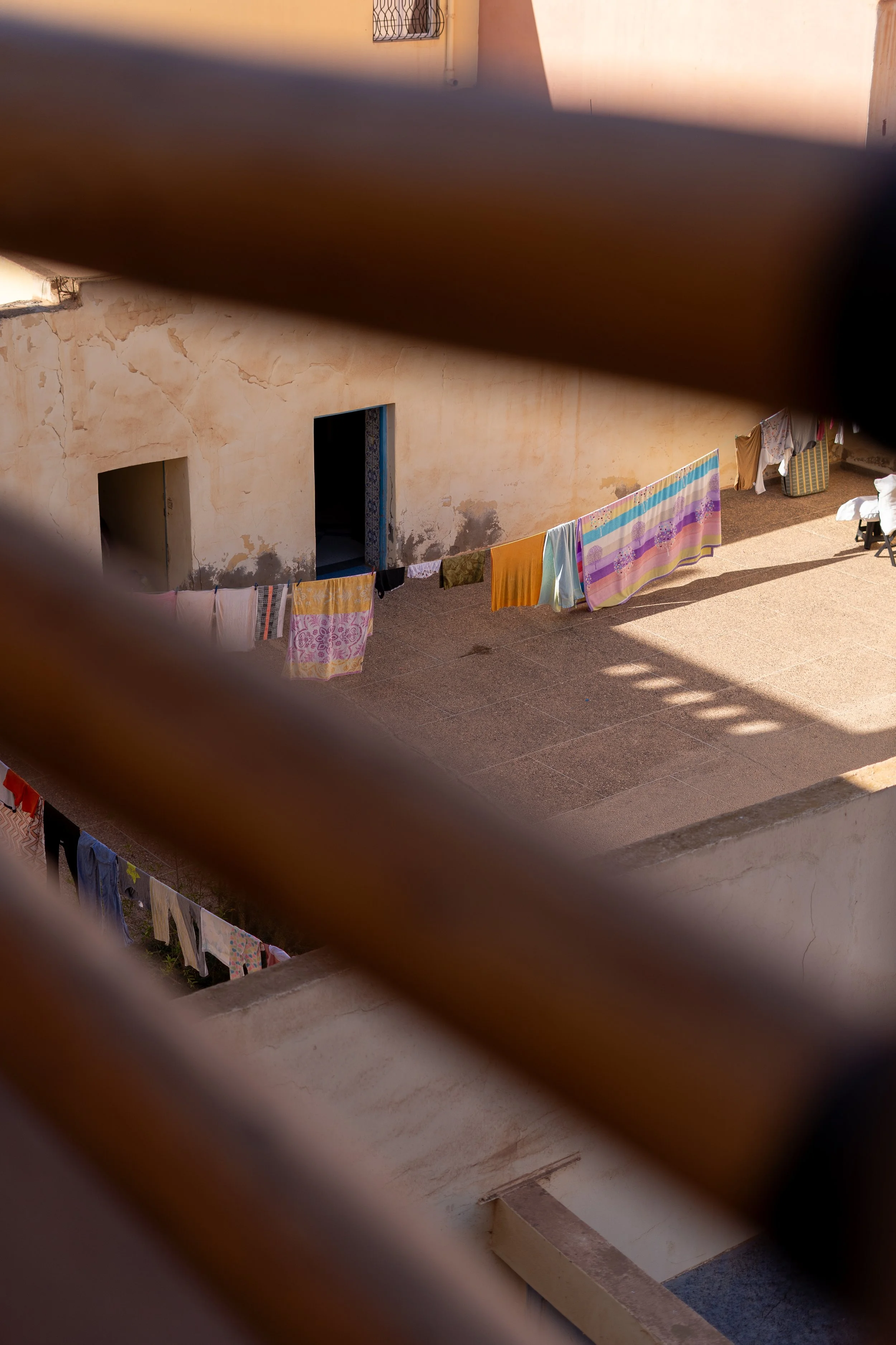 Vues d'une cour intérieure vue à travers des barres en bois ou en métal, avec des vêtements suspendus pour sécher.