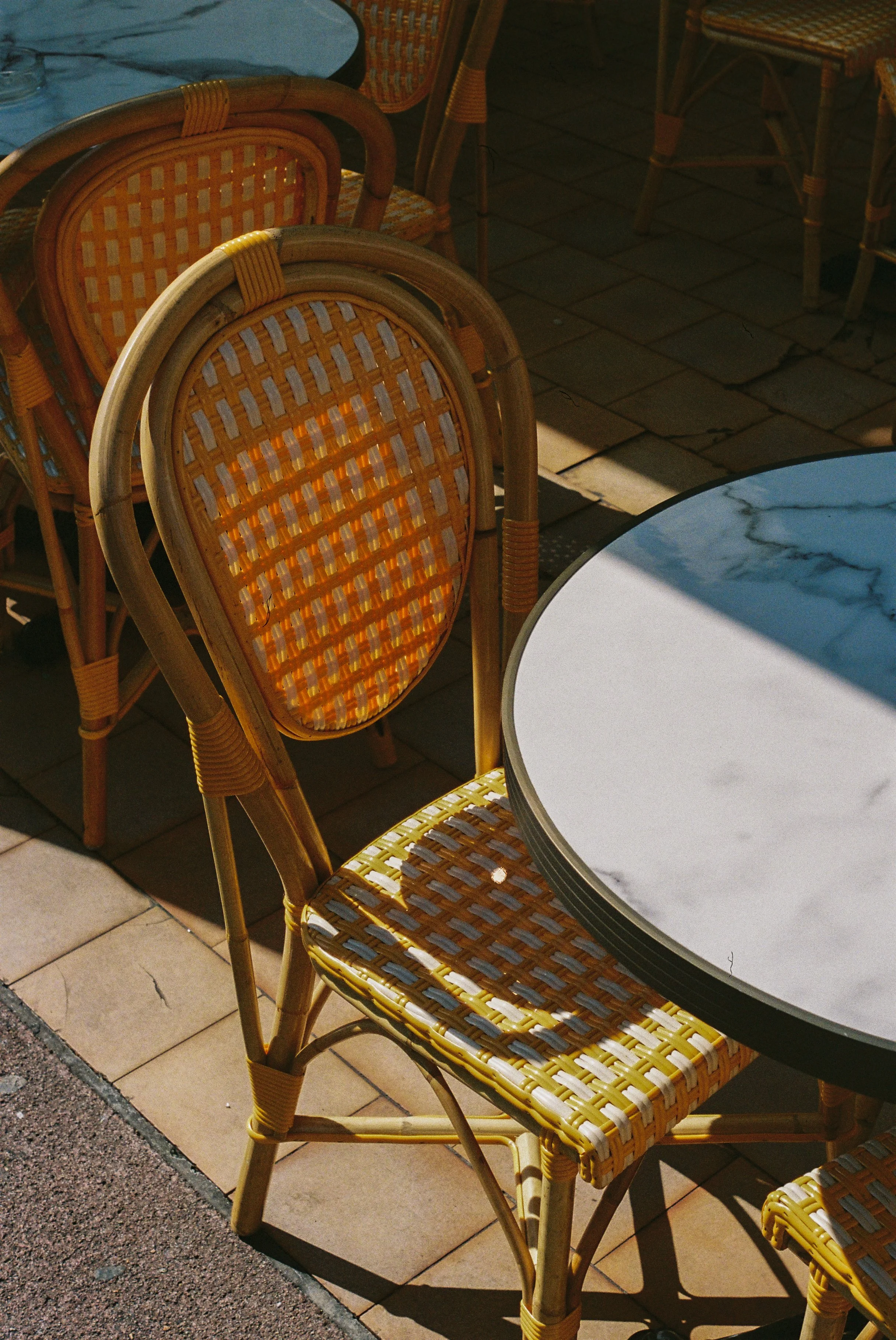 Chaises en rotin autour d'une table en marbre à l'extérieur, éclairées par le soleil.