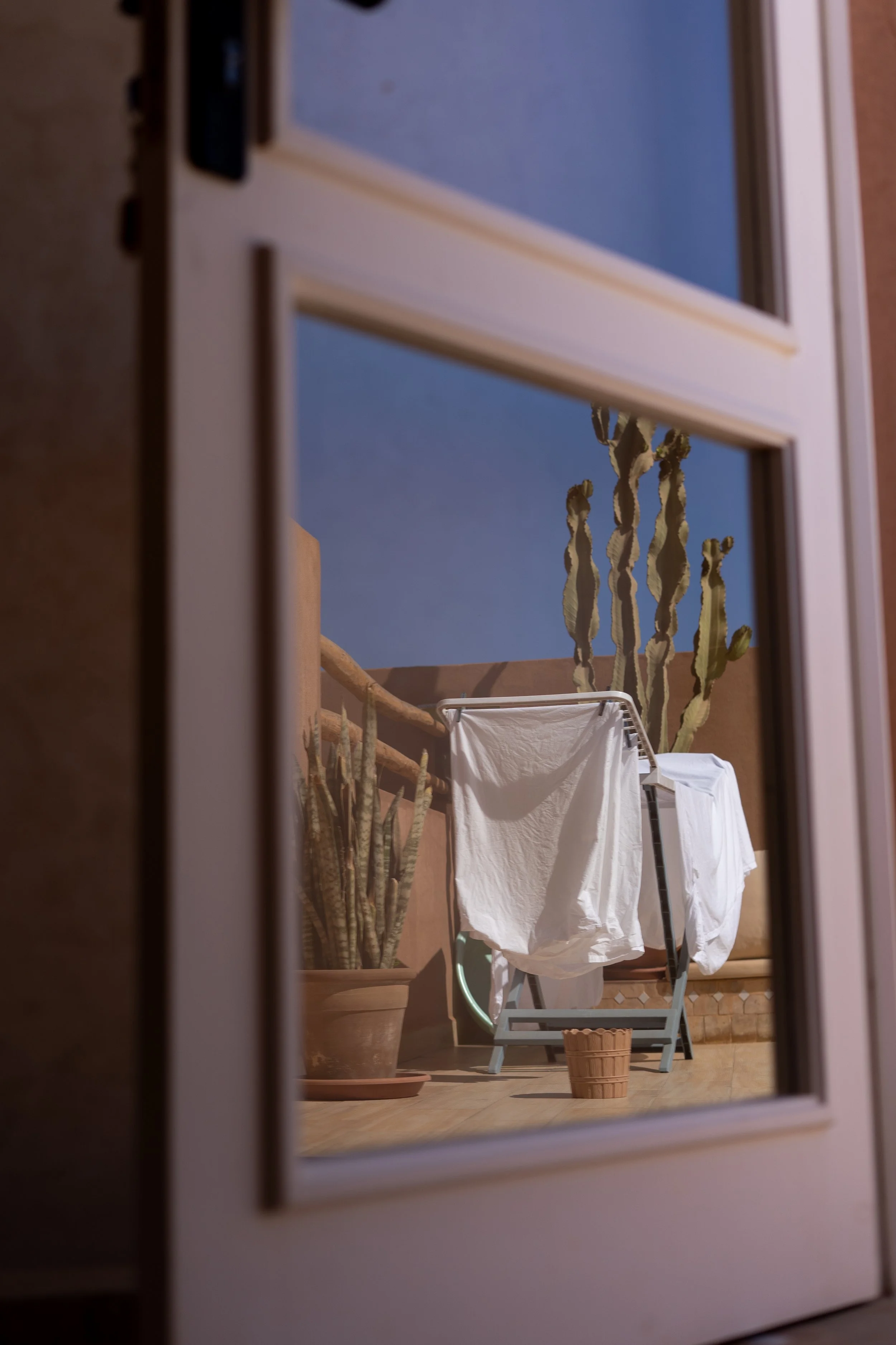 Vêtements blancs séchant à l'extérieur, vue à travers une porte en verre, avec des cactus en arrière-plan.