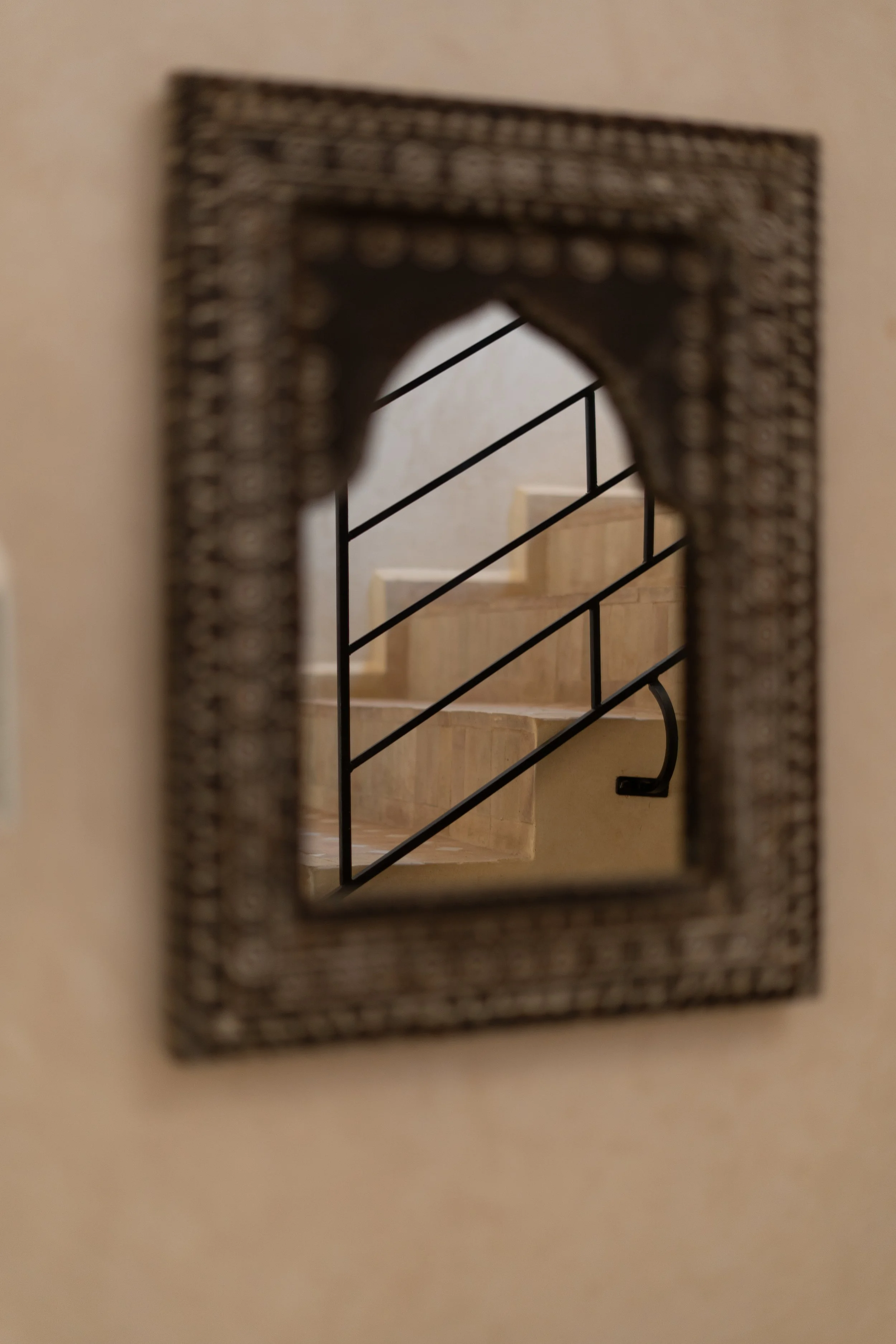 Vue à travers un miroir avec cadre décoratif, montrant un escalier en pierre avec une rampe en métal noir.