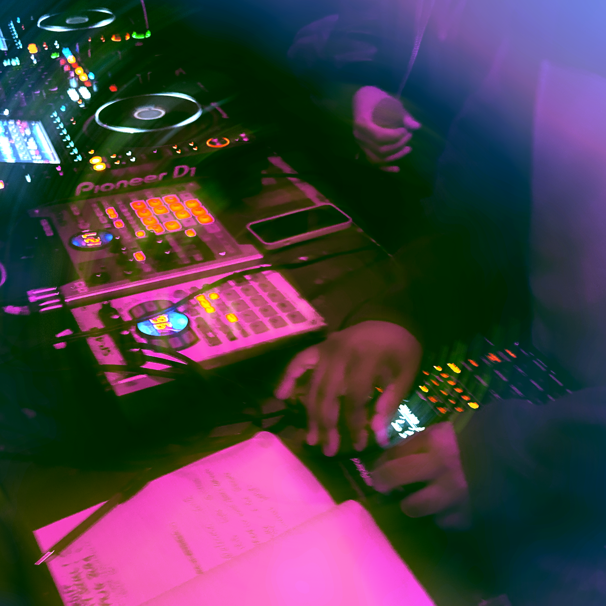 A DJ setup with a Pioneer DJ controller illuminated by colorful LED lights. The scene has a vibrant, neon aesthetic with purple, pink, and green hues.