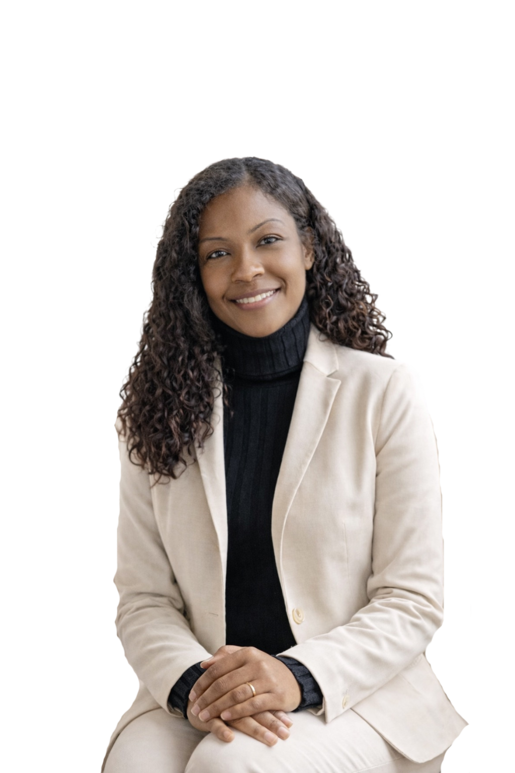 A woman with long curly brown hair smiling, wearing a black blazer over a white shirt, sitting with her hands folded in her lap.