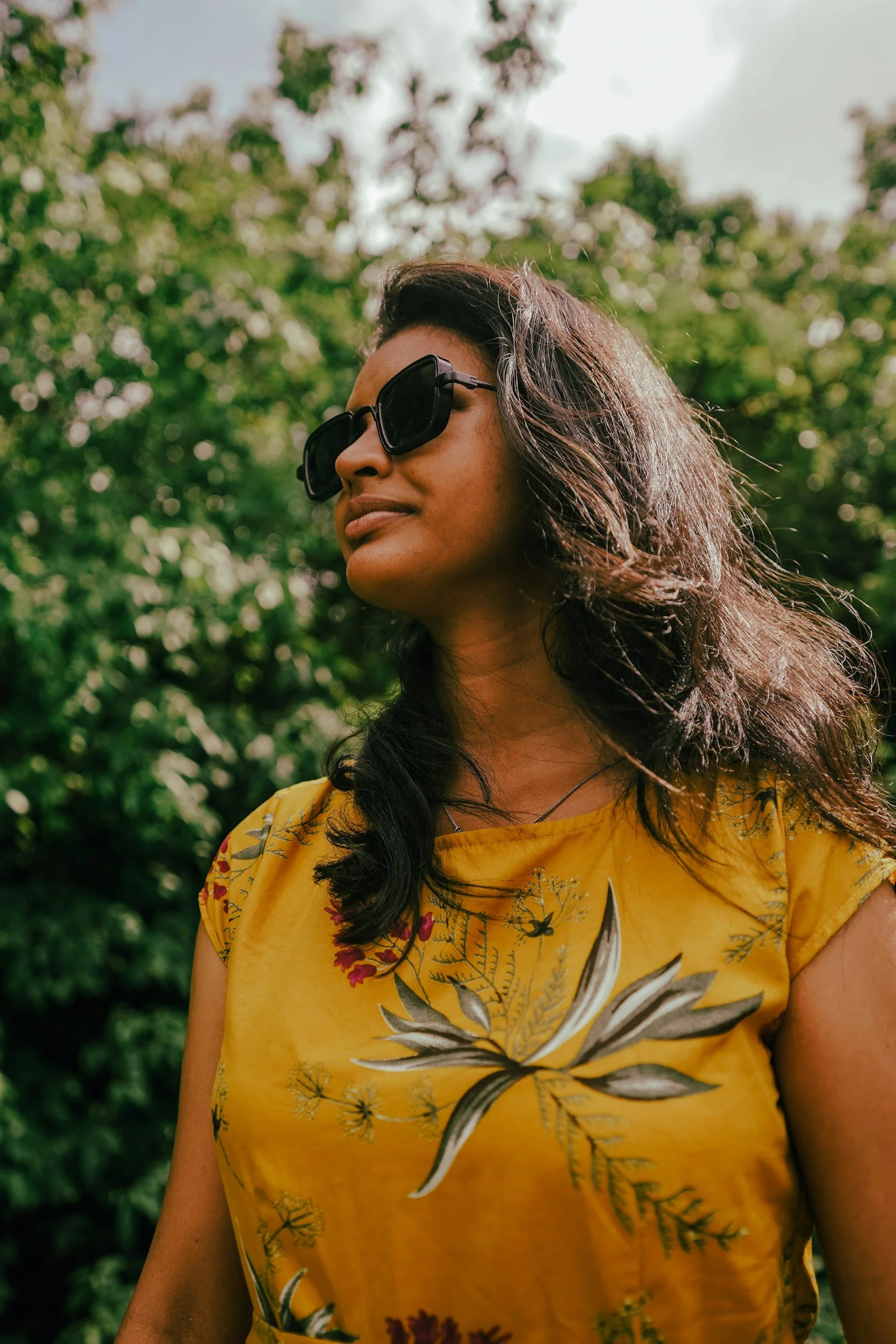 young woman in sunglass and a yellow shirt stares off